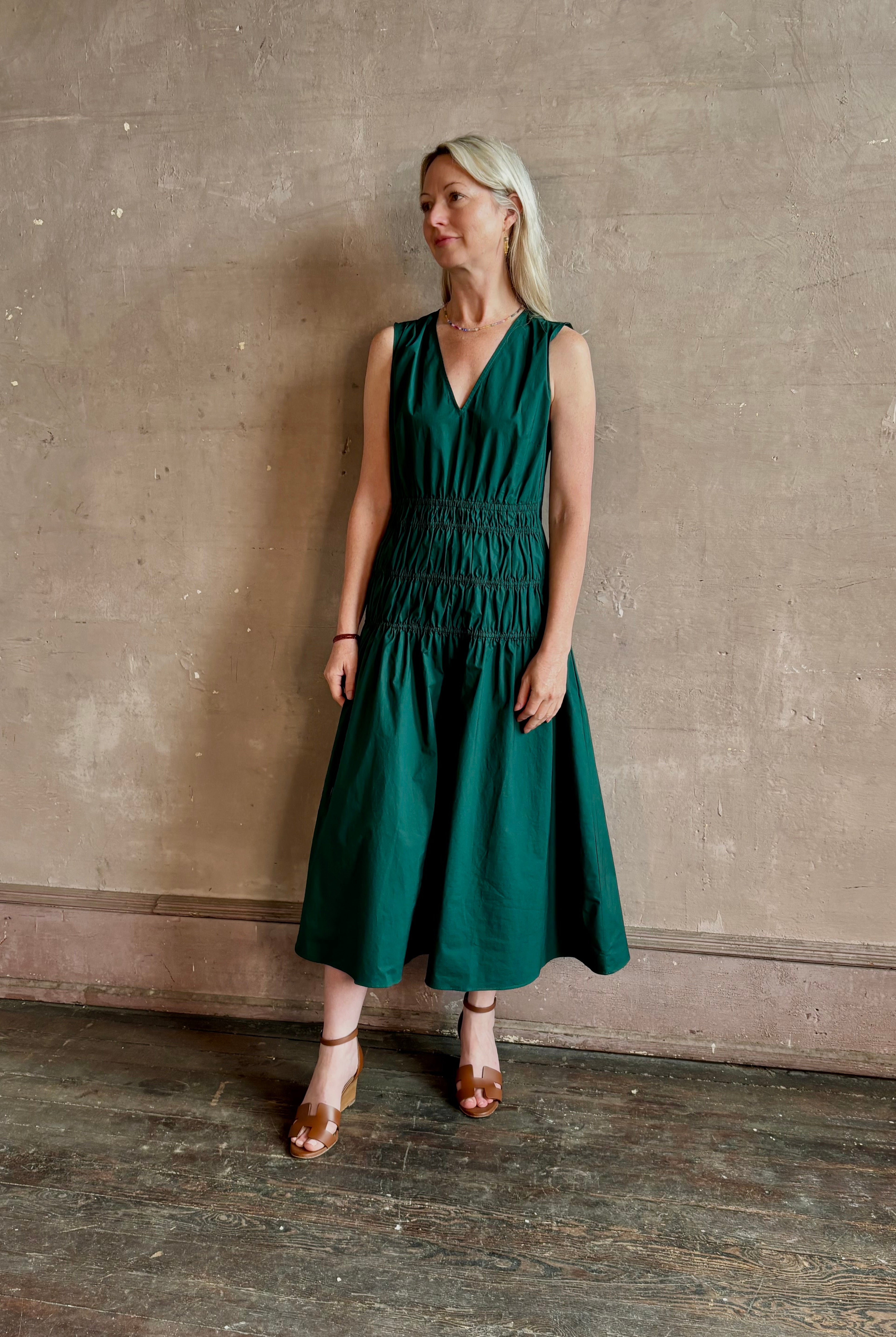 Mature woman wearing Loren Dress from Proenza Schouler White Lable rendered in aspruce green and crafted from a cotton elastane blend with v-neck, sleeveless, pockets, and rushed waist