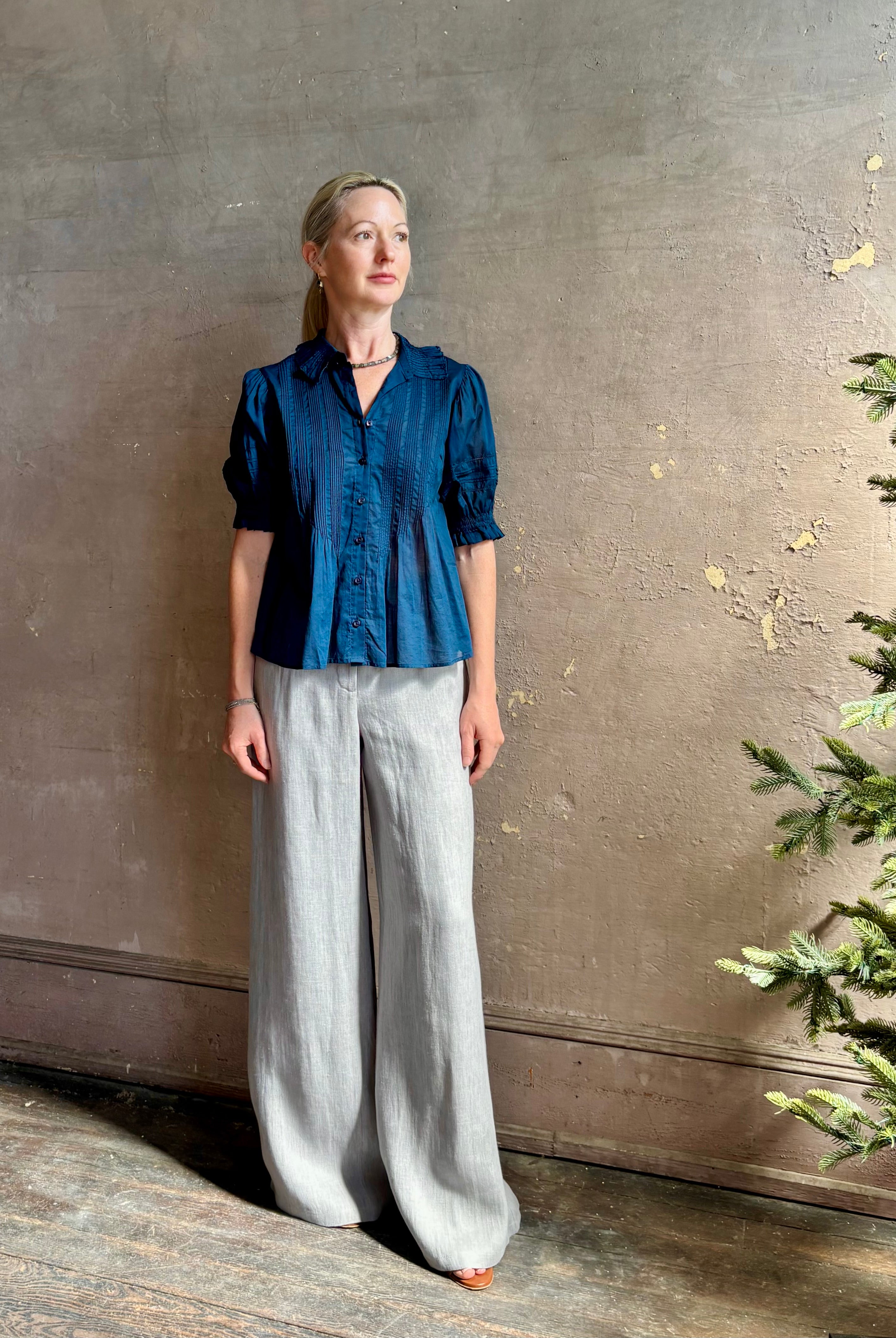 Mature woman wearing Jess Blouse from Trovata rendered in a classic Navy blue and crafted from light weight cotton poplin with short sleeves, peter pan collar, v-neck button front with intricate pintucking details at front and back