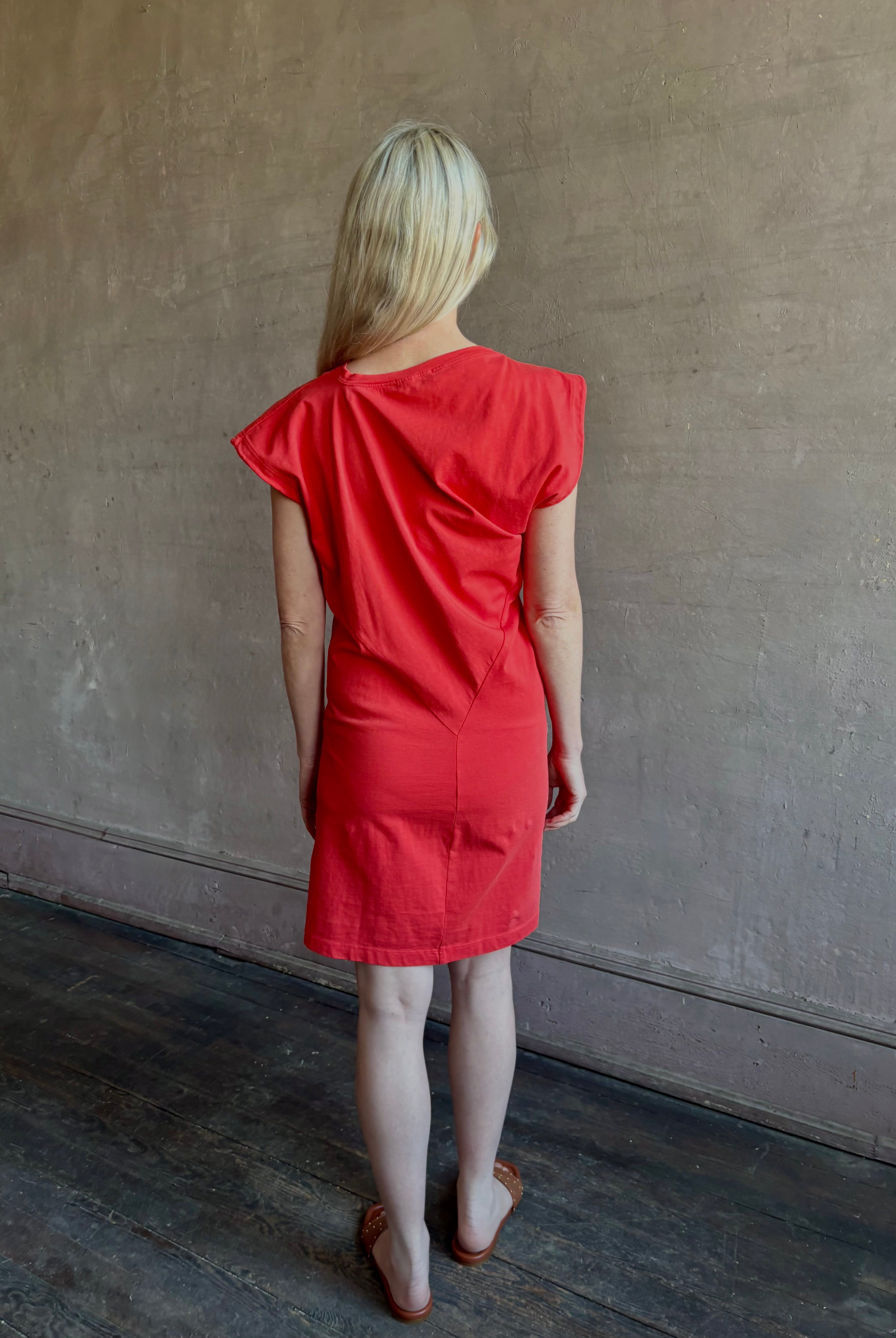 Woman wearing the red Beth Dress from Agolde crafted from 100% cotton with short sleeves, knee length and asymmetrical twist draping in a effortless relaxed fit