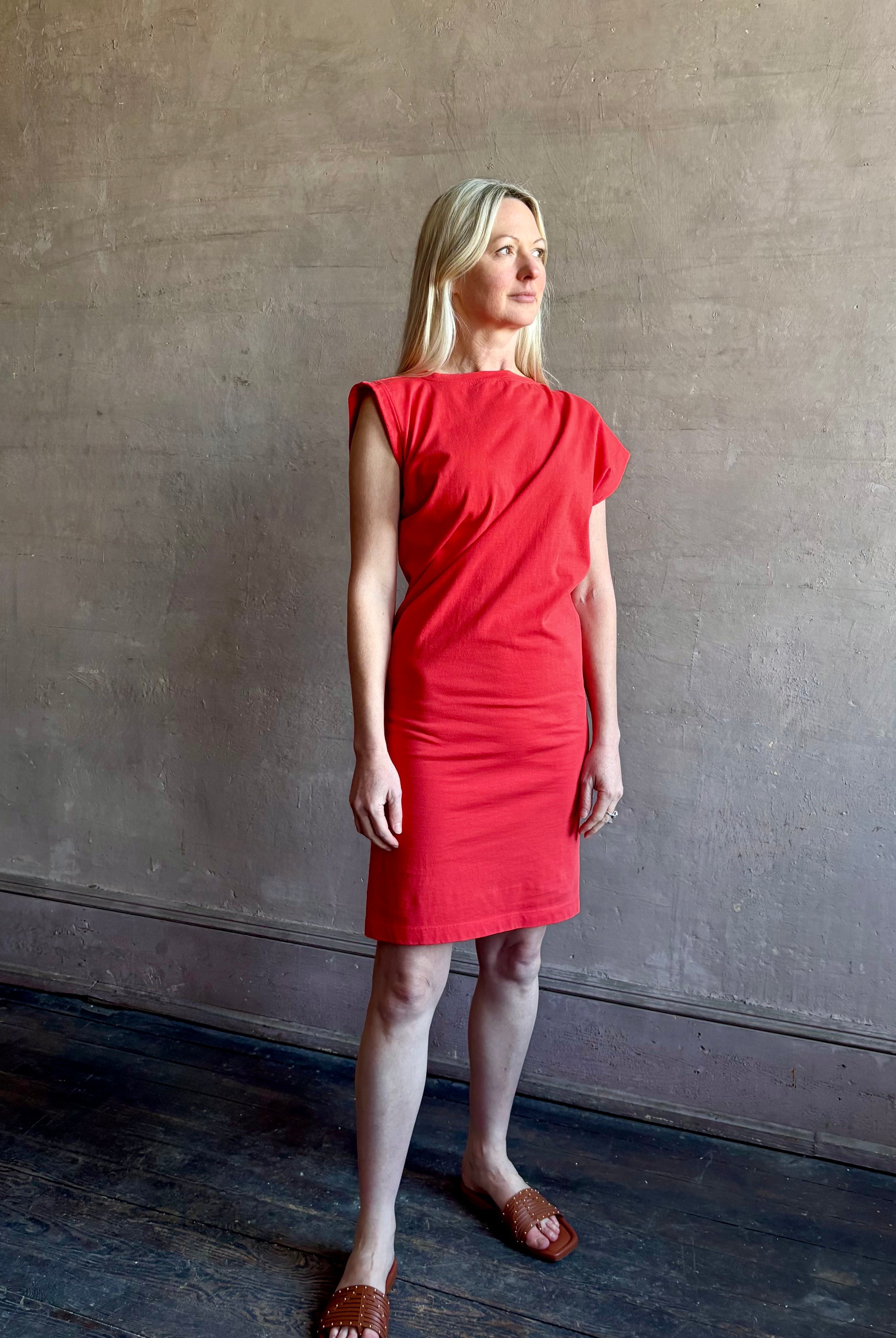 Woman wearing the red Beth Dress from Agolde crafted from 100% cotton with short sleeves, knee length and asymmetrical twist draping in a effortless relaxed fit