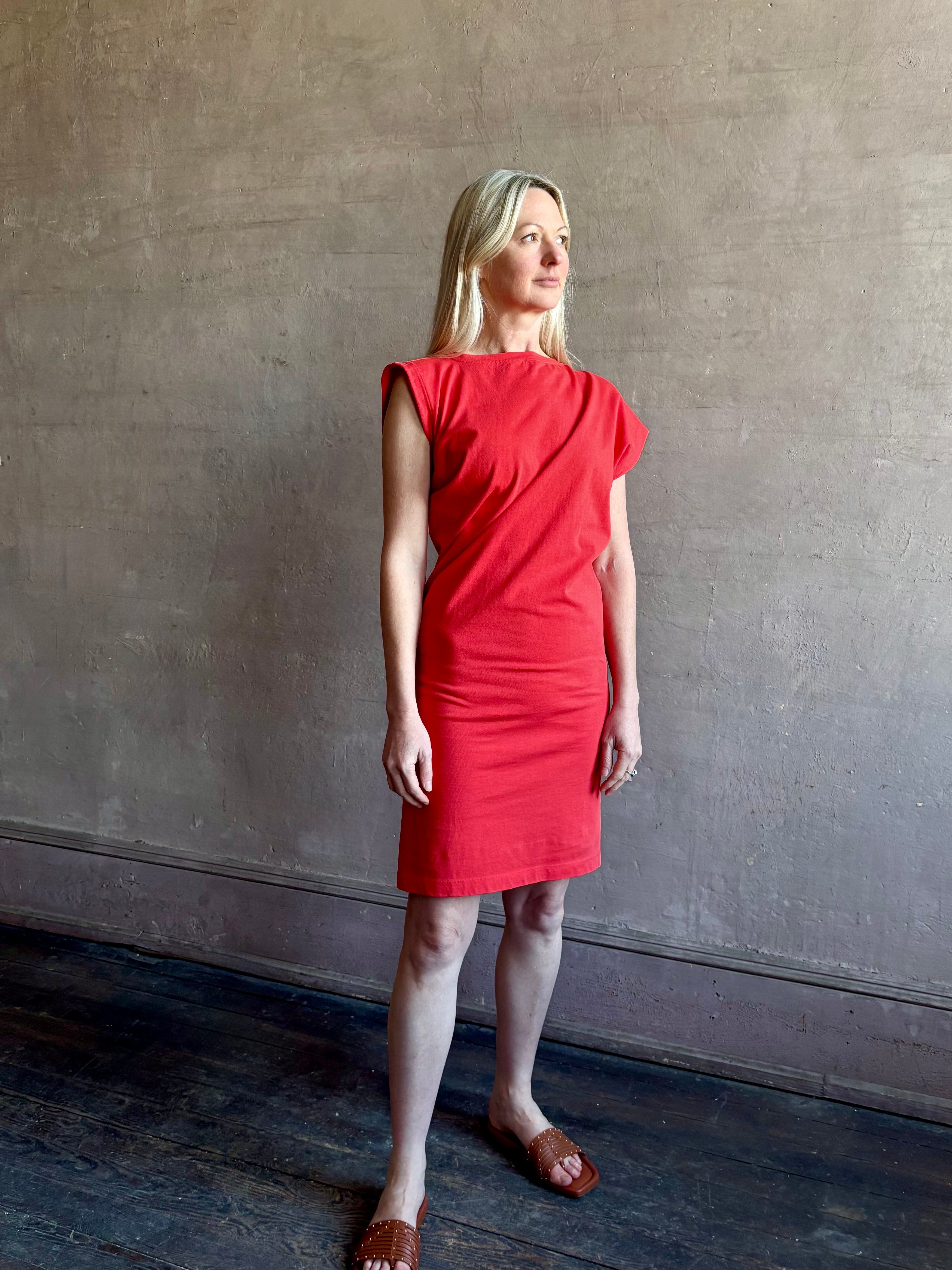 Woman wearing the red Beth Dress from Agolde crafted from 100% cotton with short sleeves, knee length and asymmetrical twist draping in a effortless relaxed fit