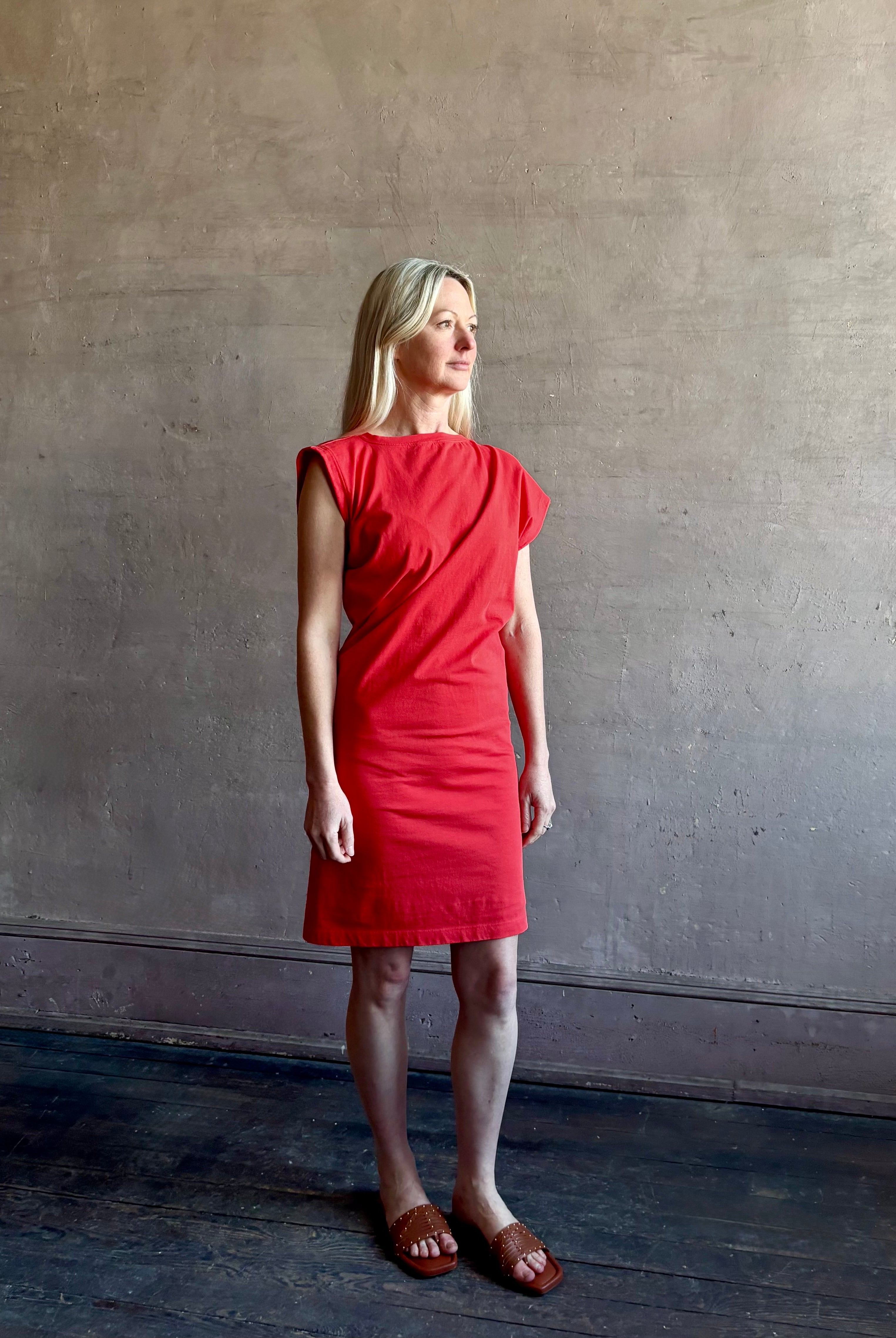 Woman wearing the red Beth Dress from Agolde crafted from 100% cotton with short sleeves, knee length and asymmetrical twist draping in a effortless relaxed fit