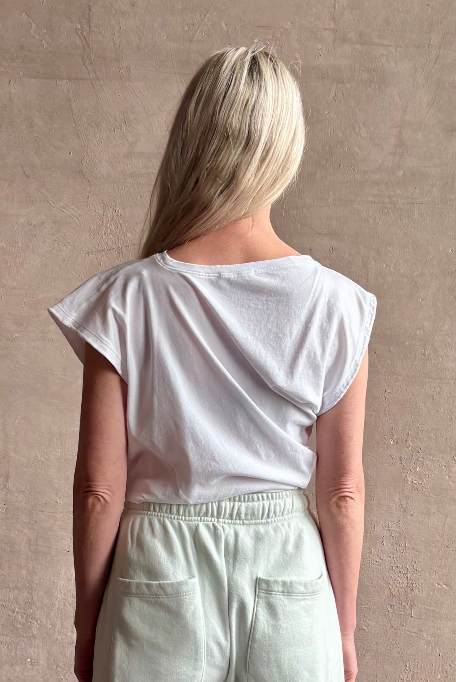 Mature woman wearing a white asymmetrical beth tee shirt from Agolde with short sleeves, crew neckline and architectural draping