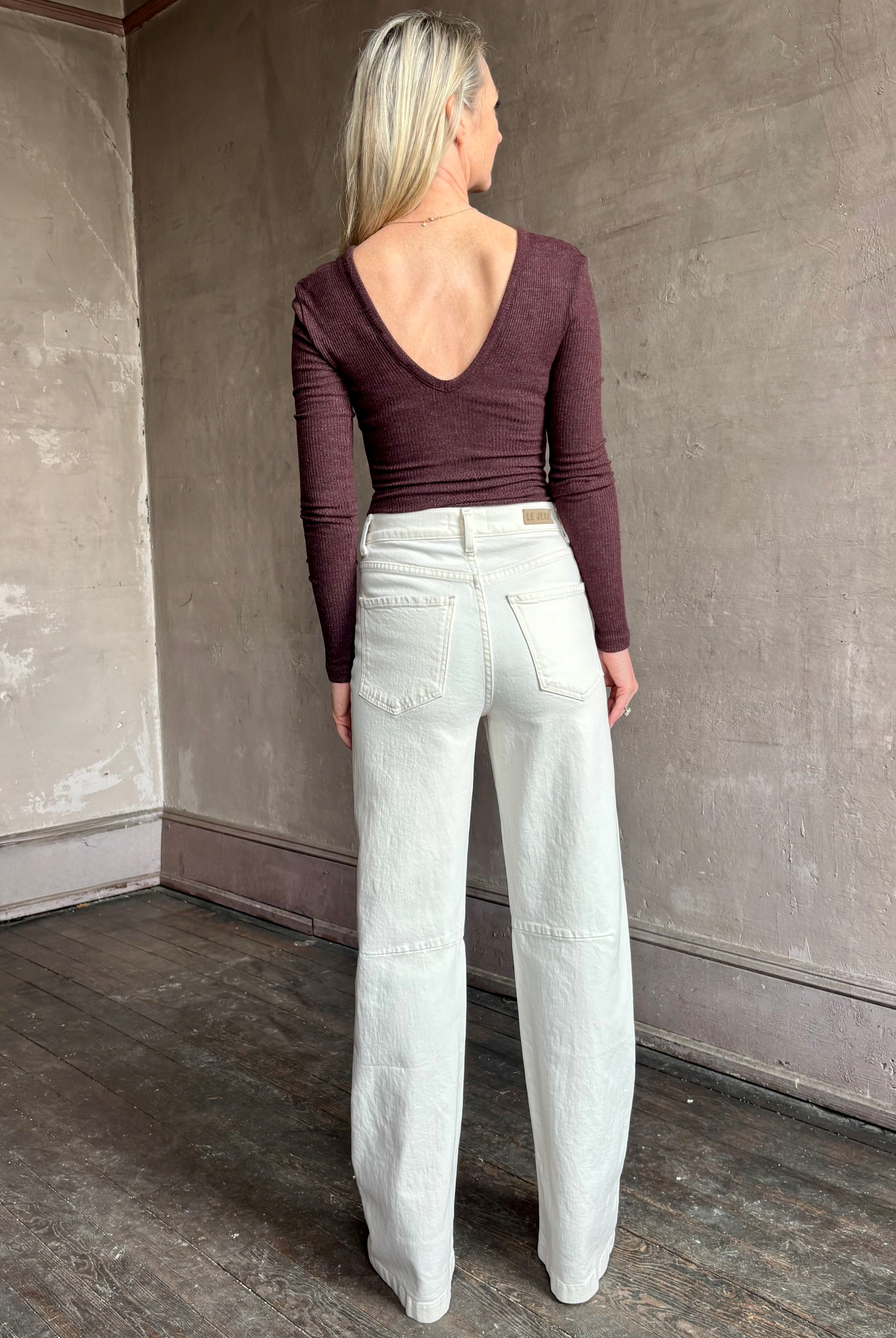 Image of woman wearing Agolde Darla Bodysuit in raisin colorway with deep v back and long sleeves perfect for layering