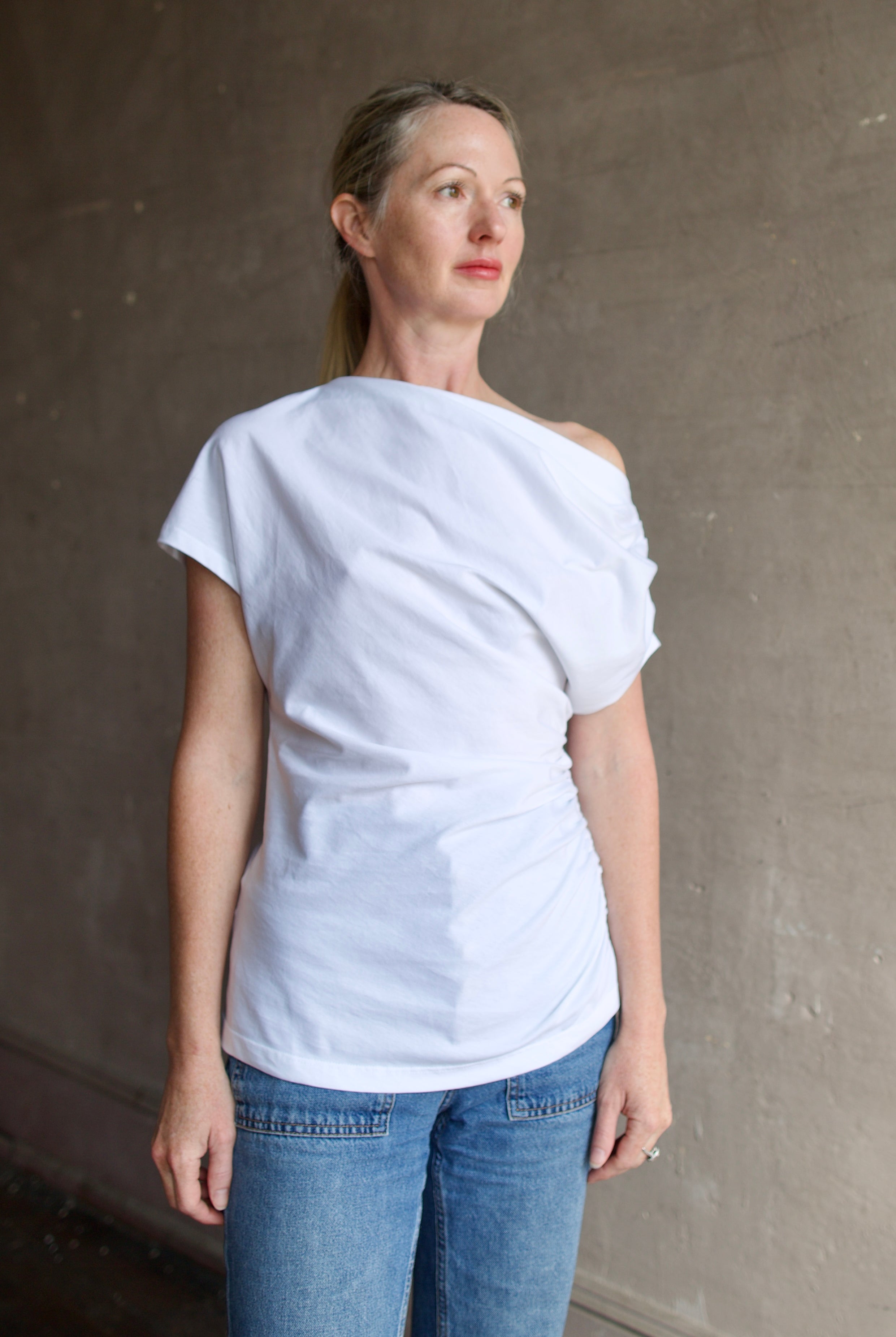 Model wearing white ALC Alice cotton t-shirt with rushed sides and shoulder detail that can be worn asymmetrically