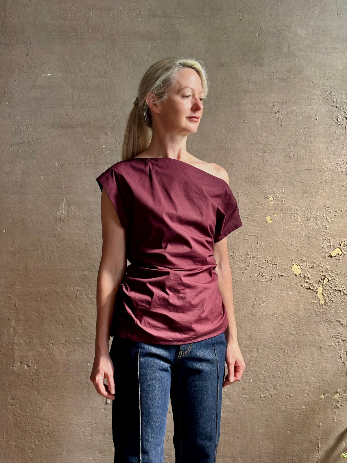 Mature woman wearing A.L.C.'s Nara Top in burgundy cotton poplin cold shoulder draping feminine cosmopolitan tailoring