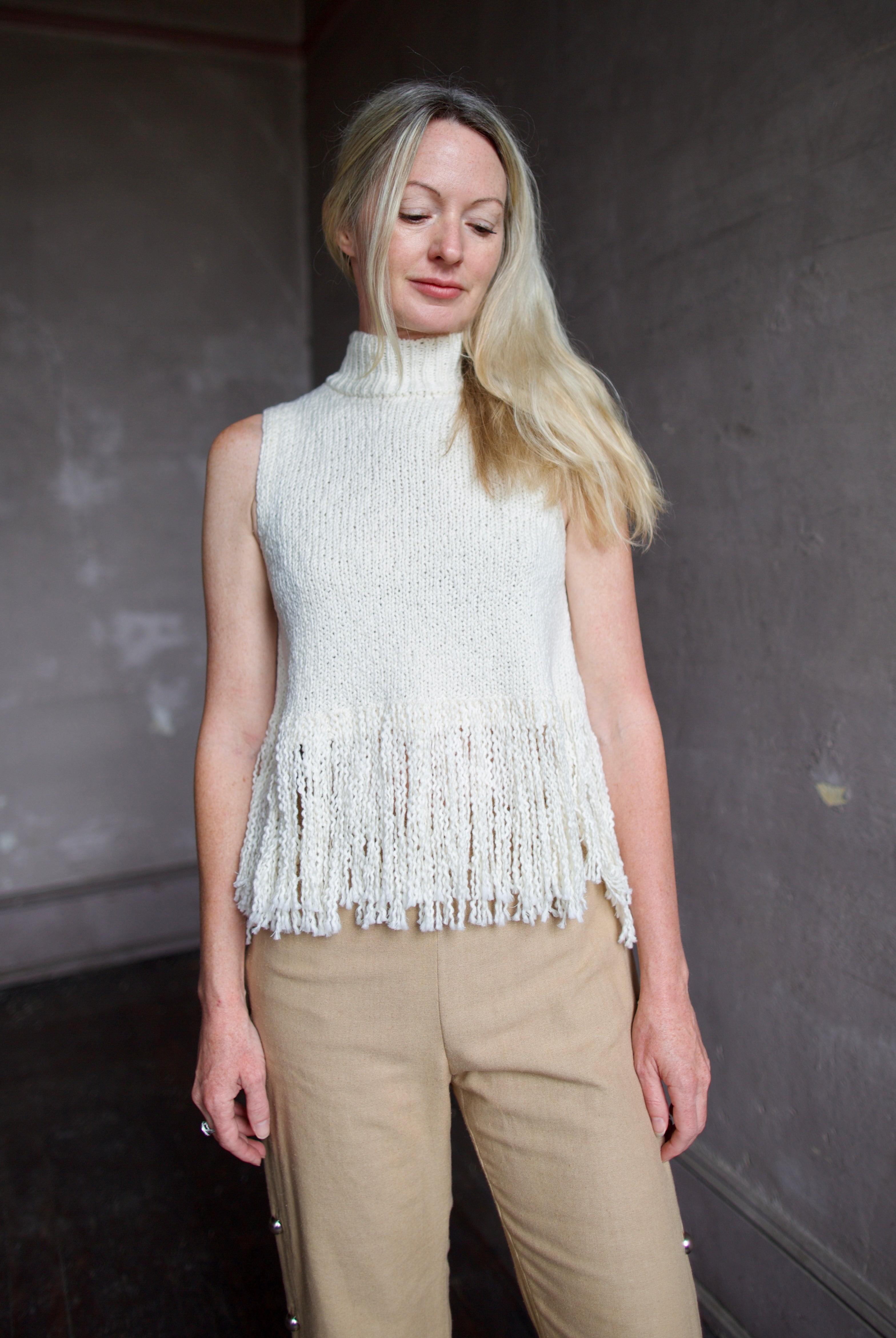 Model wearing an Alix of Bohemia cream sleeveless cotton sweater with fringe trimmed top