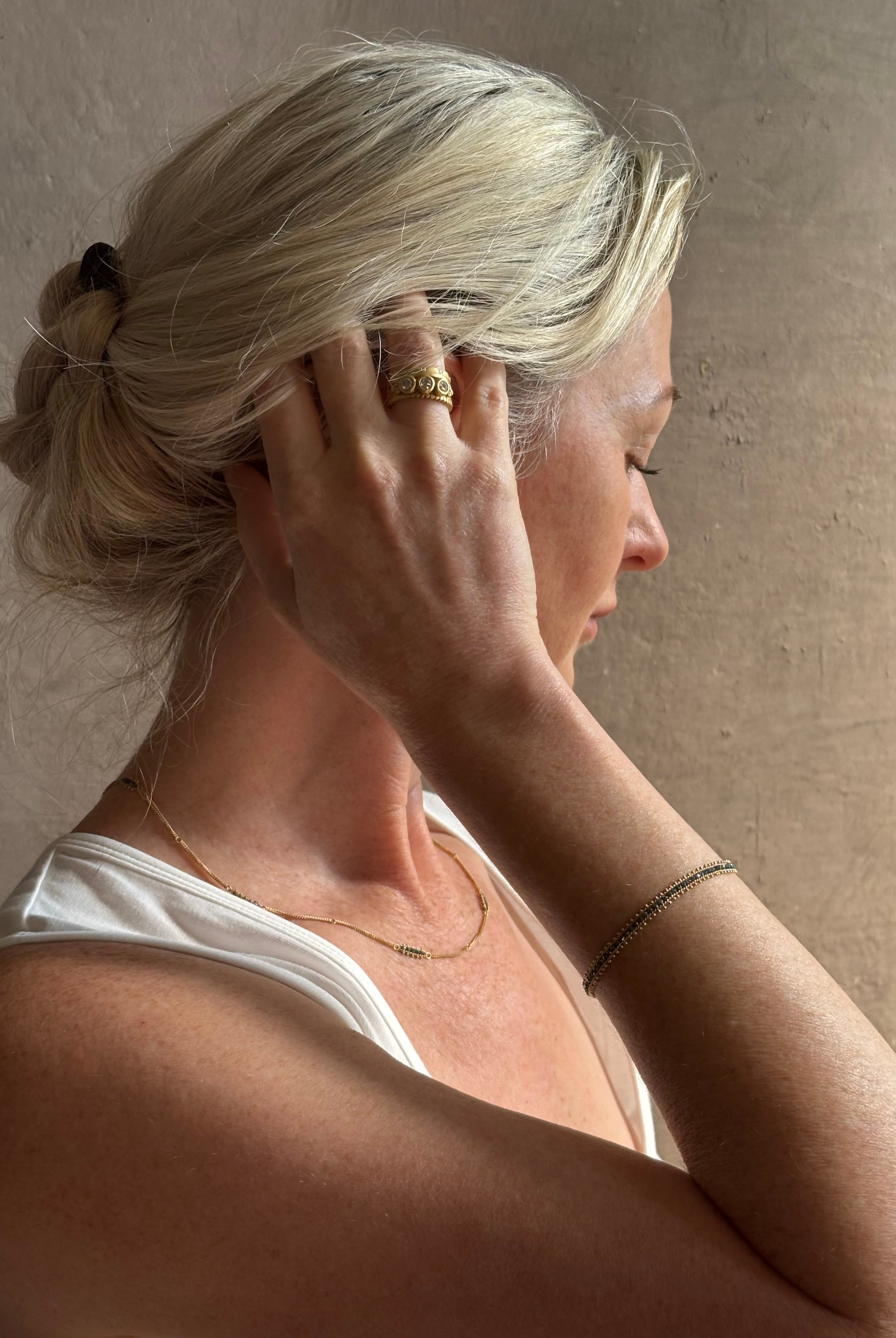 Mature woman wearing a vivid natural blue diamond row bracelet designed by NC fine jeweler Amali in warm 18K yellow gold