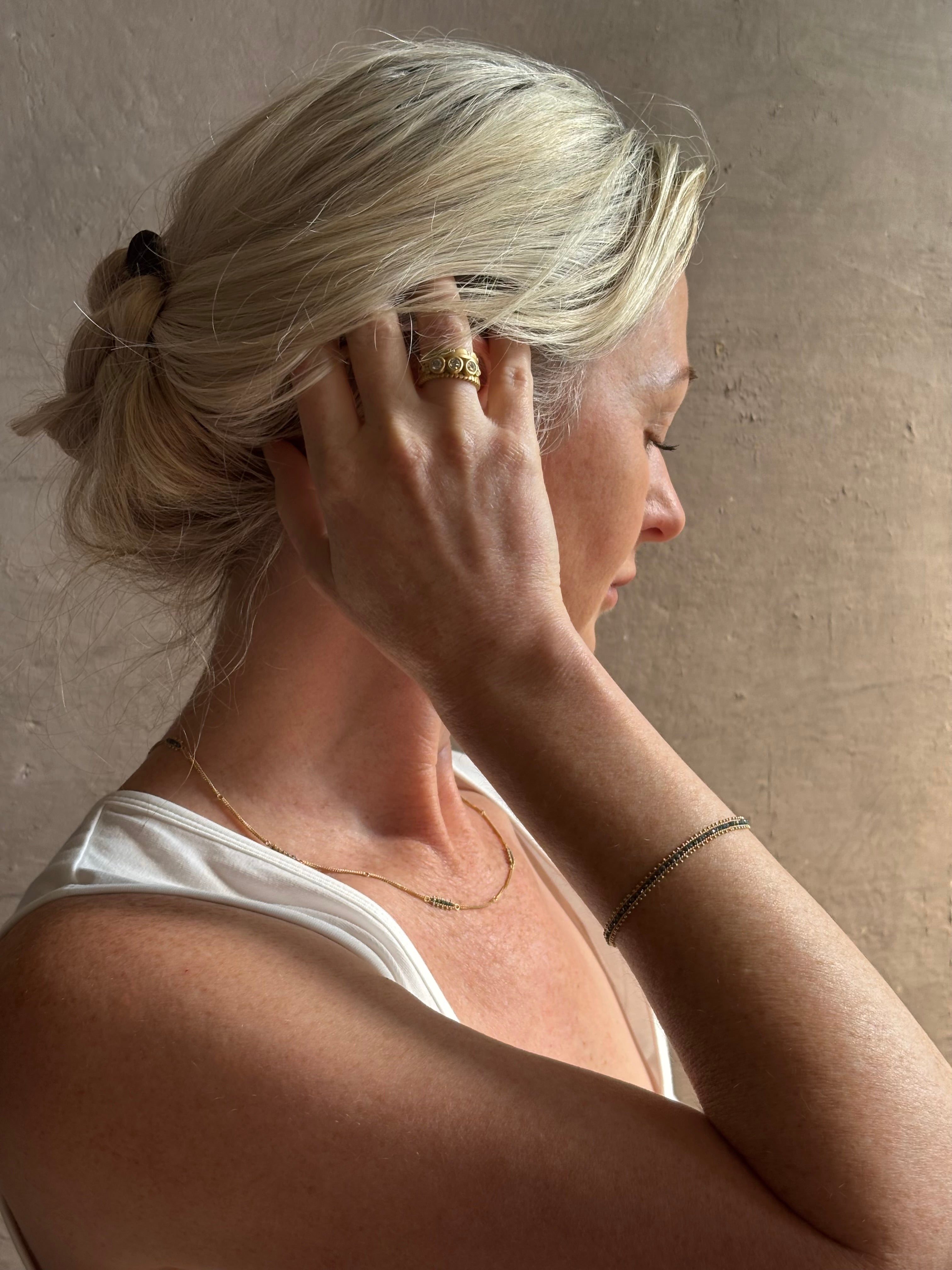 Mature woman wearing a vivid natural blue diamond row bracelet designed by NC fine jeweler Amali in warm 18K yellow gold