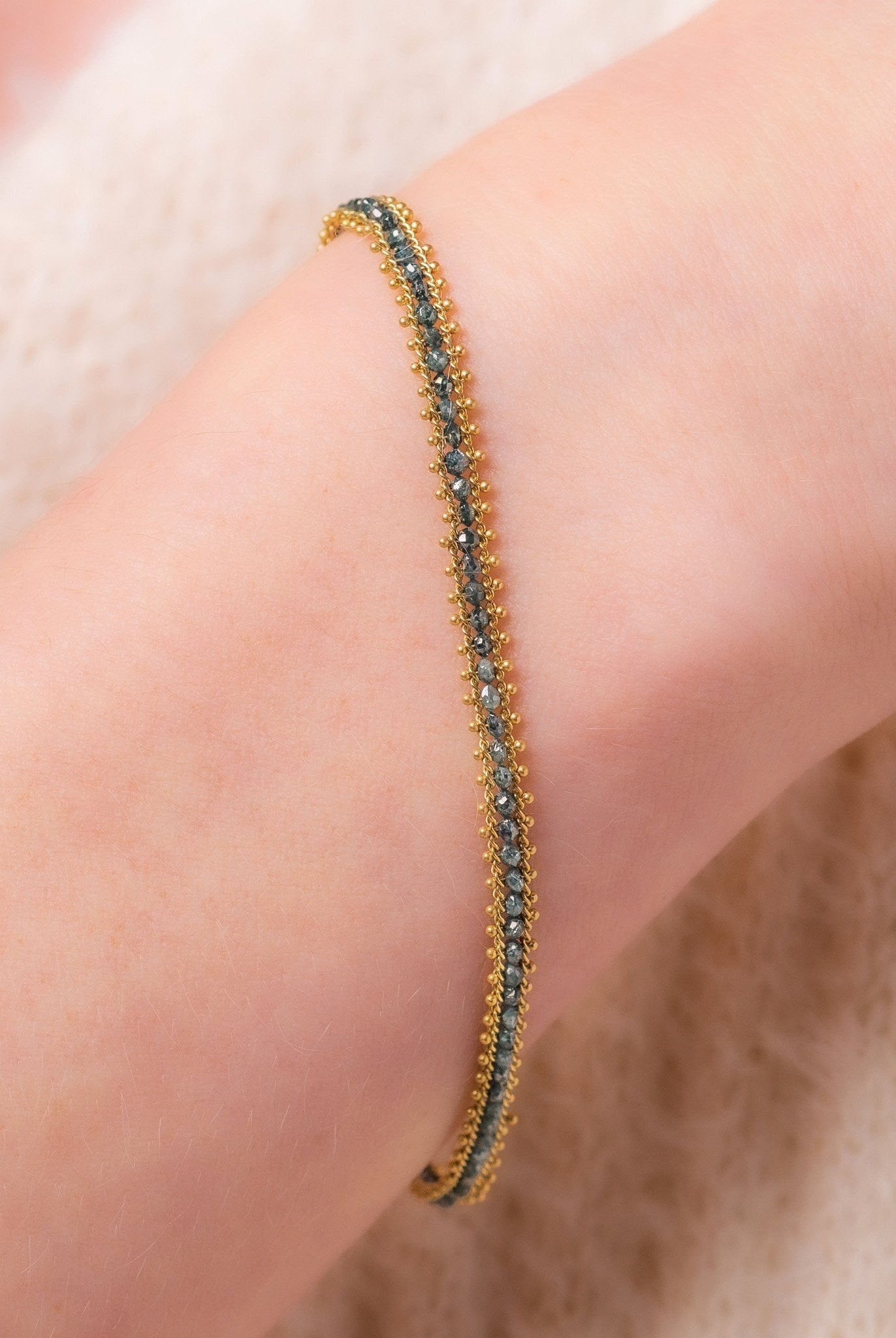 Image of a woman wearing a vivid natural blue diamond row bracelet designed by NC fine jeweler Amali in warm 18K yellow gold