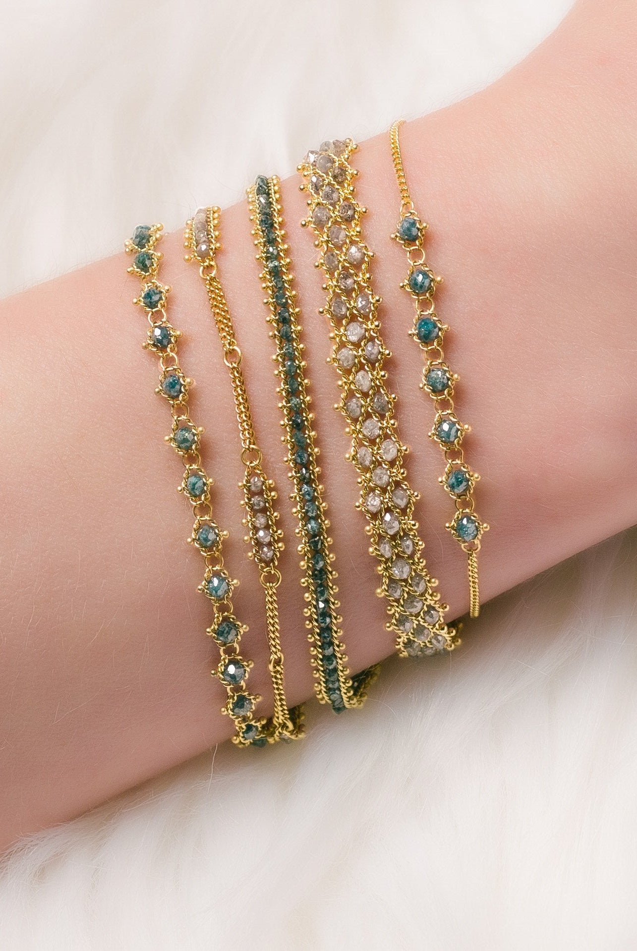 Photo of a woman wearing a stack of luxury silver and blue natural diamond bracelets designed by NC fine jeweler Amali in warm 18K yellow gold