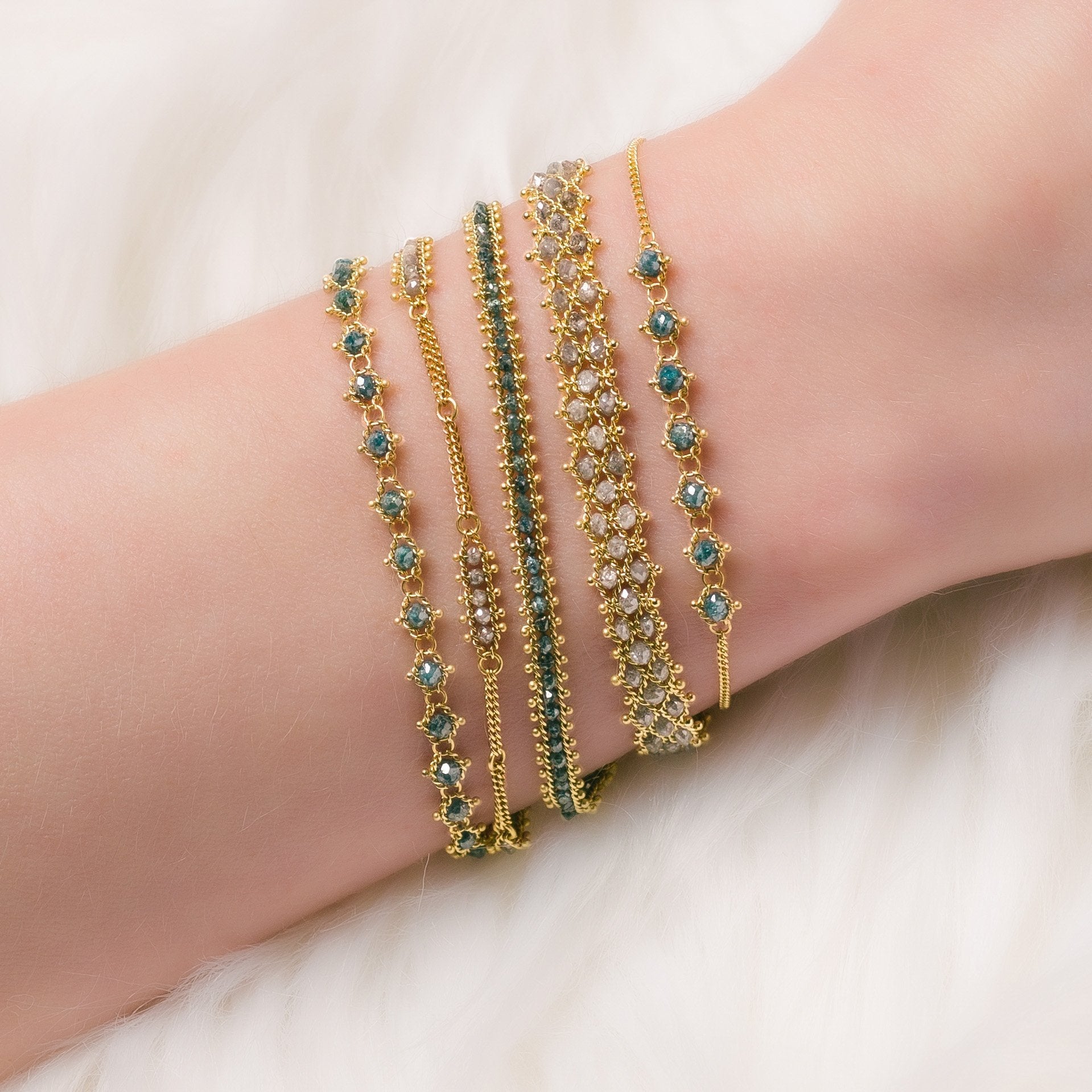 Photo of a woman wearing a stack of luxury silver and blue natural diamond bracelets designed by NC fine jeweler Amali in warm 18K yellow gold