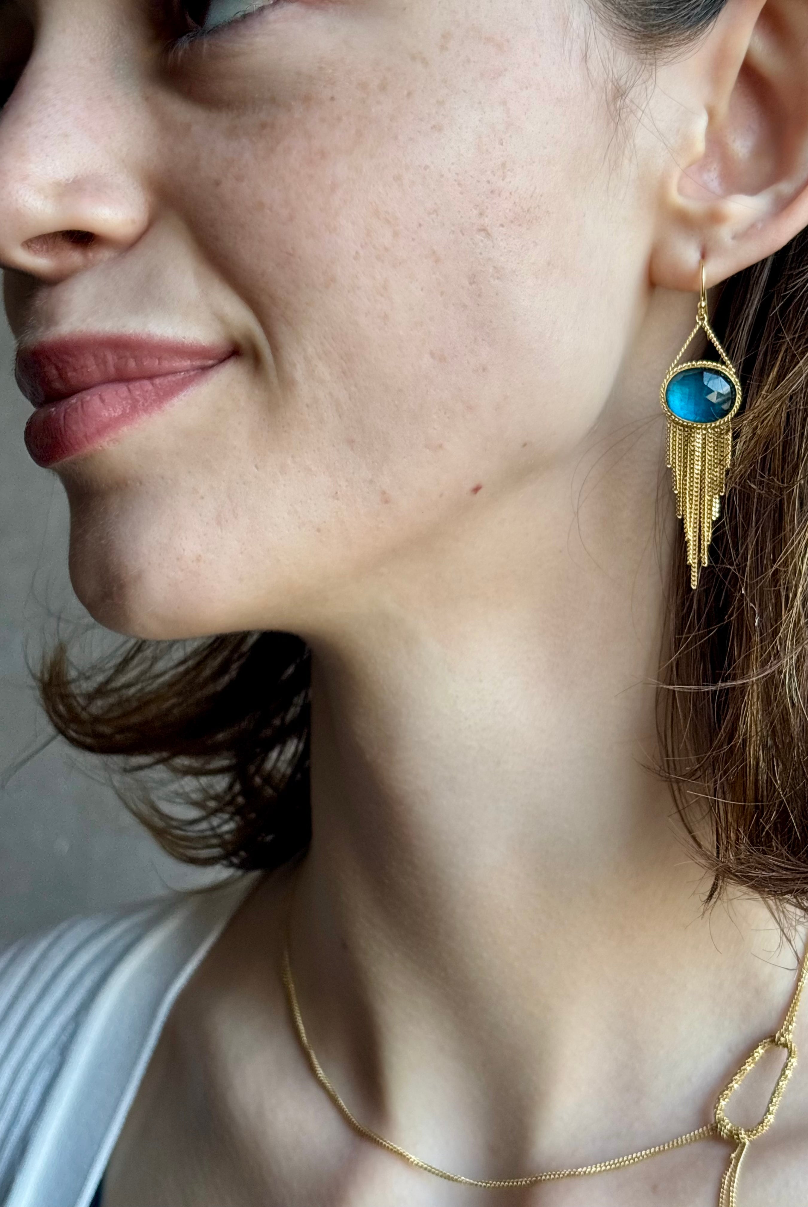 Woman wearing the London Blue Topaz statement drop Earrings from Amali are handcrafted in New York with 18K yellow gold with kinetic gold fringe detail finish at bottom