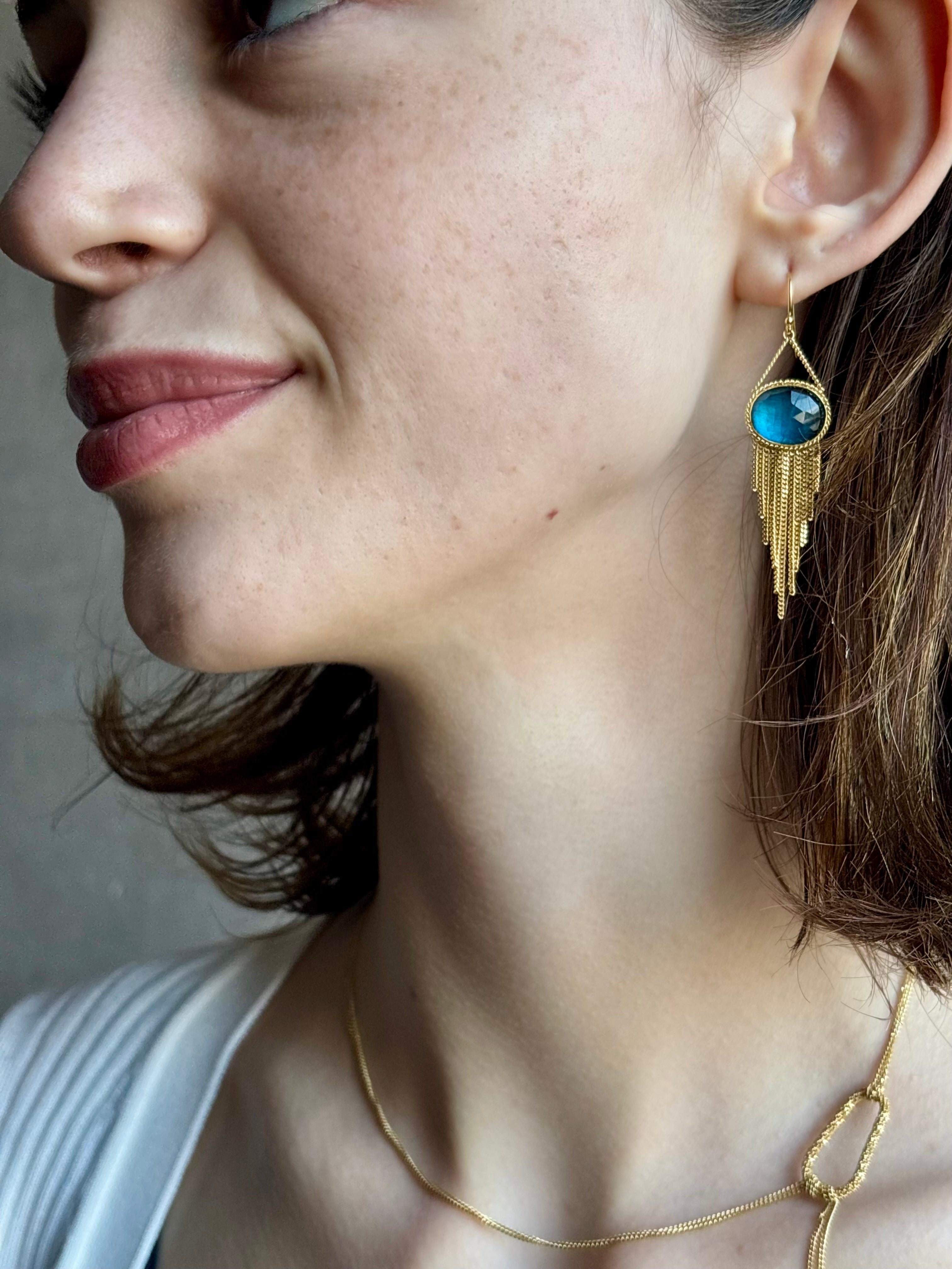 Woman wearing the London Blue Topaz statement drop Earrings from Amali are handcrafted in New York with 18K yellow gold with kinetic gold fringe detail finish at bottom