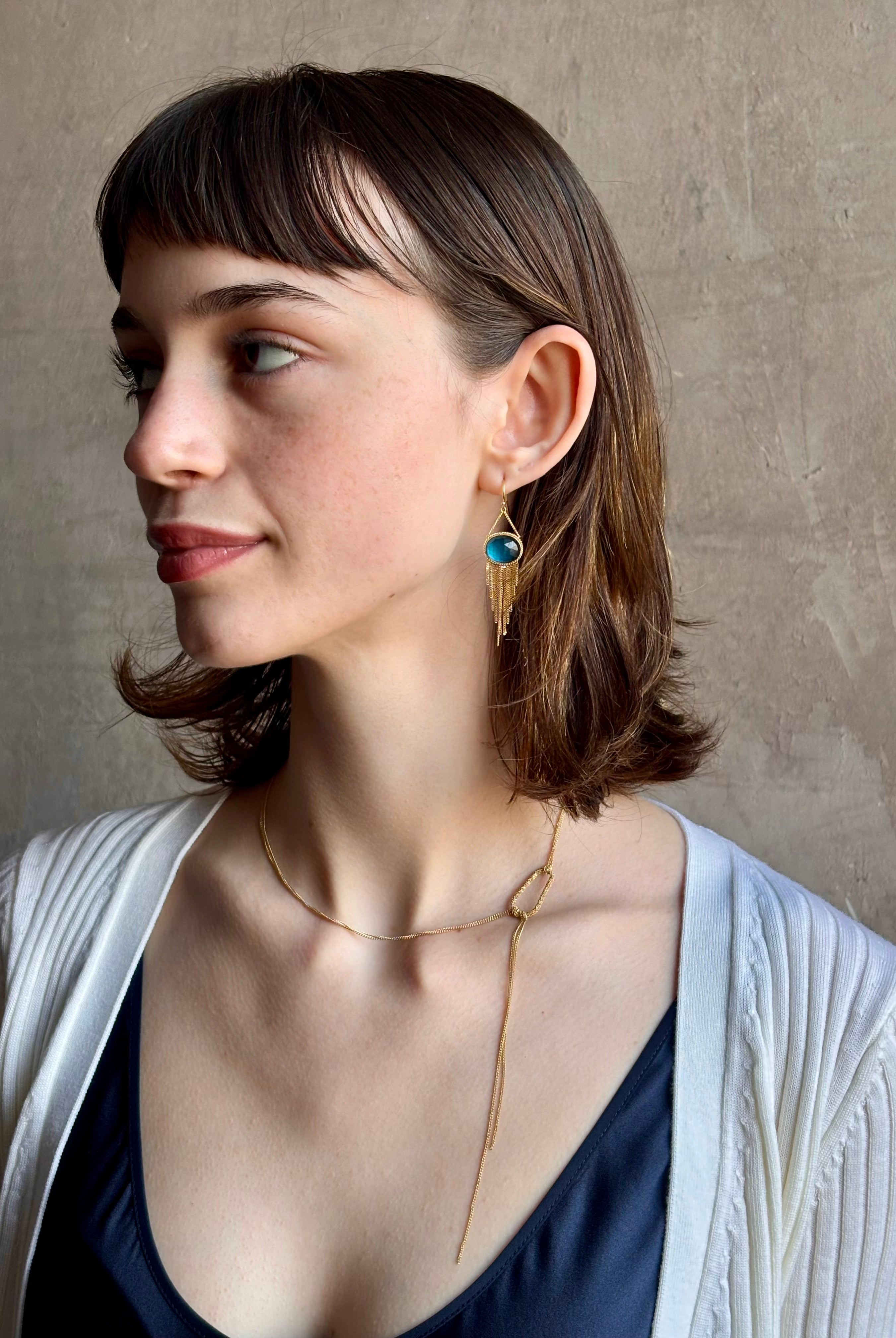Woman wearing the London Blue Topaz statement drop Earrings from Amali are handcrafted in New York with 18K yellow gold with kinetic gold fringe detail finish at bottom