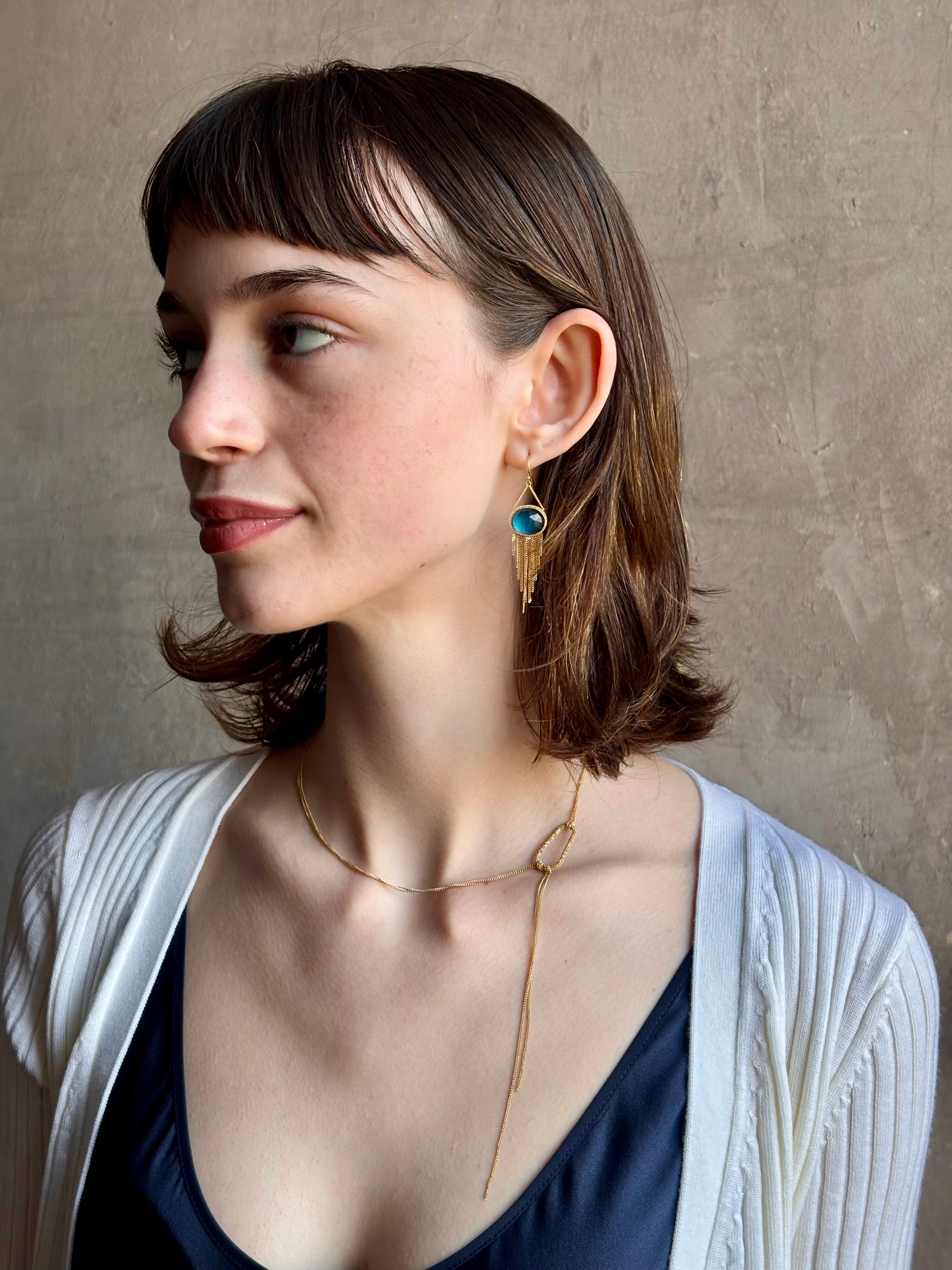Woman wearing the London Blue Topaz statement drop Earrings from Amali are handcrafted in New York with 18K yellow gold with kinetic gold fringe detail finish at bottom