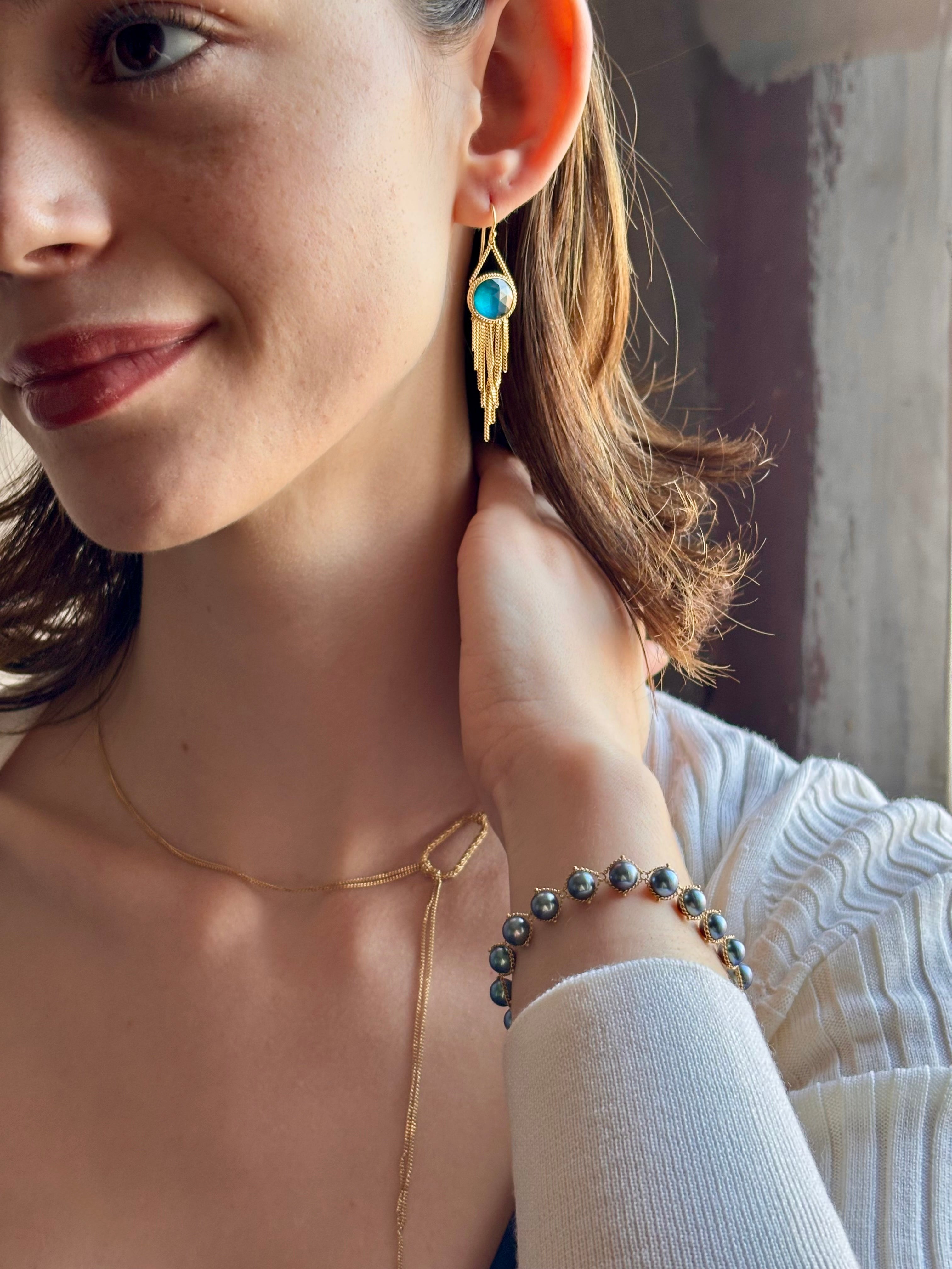 Woman wearing the London Blue Topaz statement drop Earrings from Amali are handcrafted in New York with 18K yellow gold with kinetic gold fringe detail finish at bottom