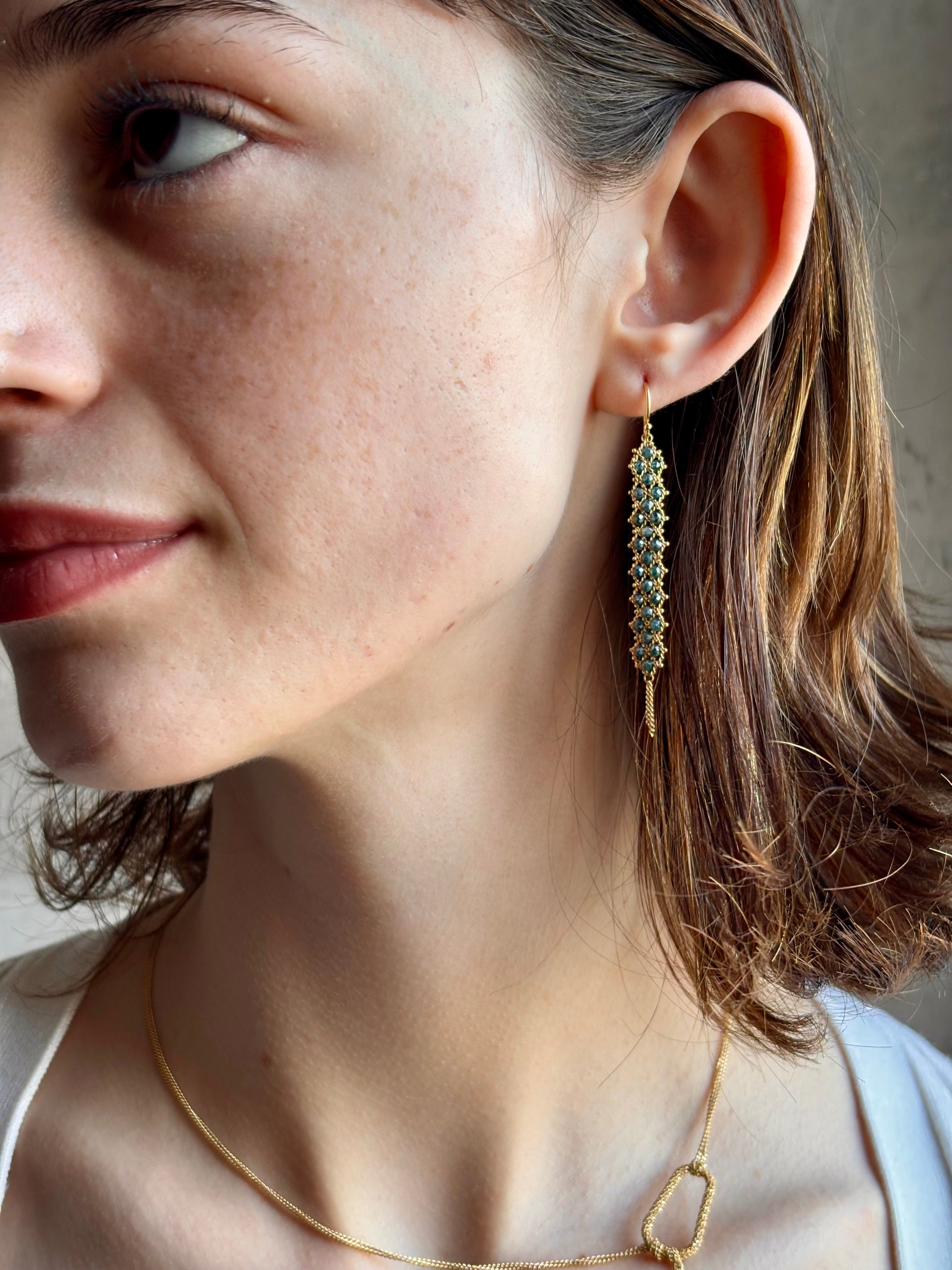 Woman wearing hand woven blue diamonds and 18k yellow gold earrings by New York jewelry designer Amali
