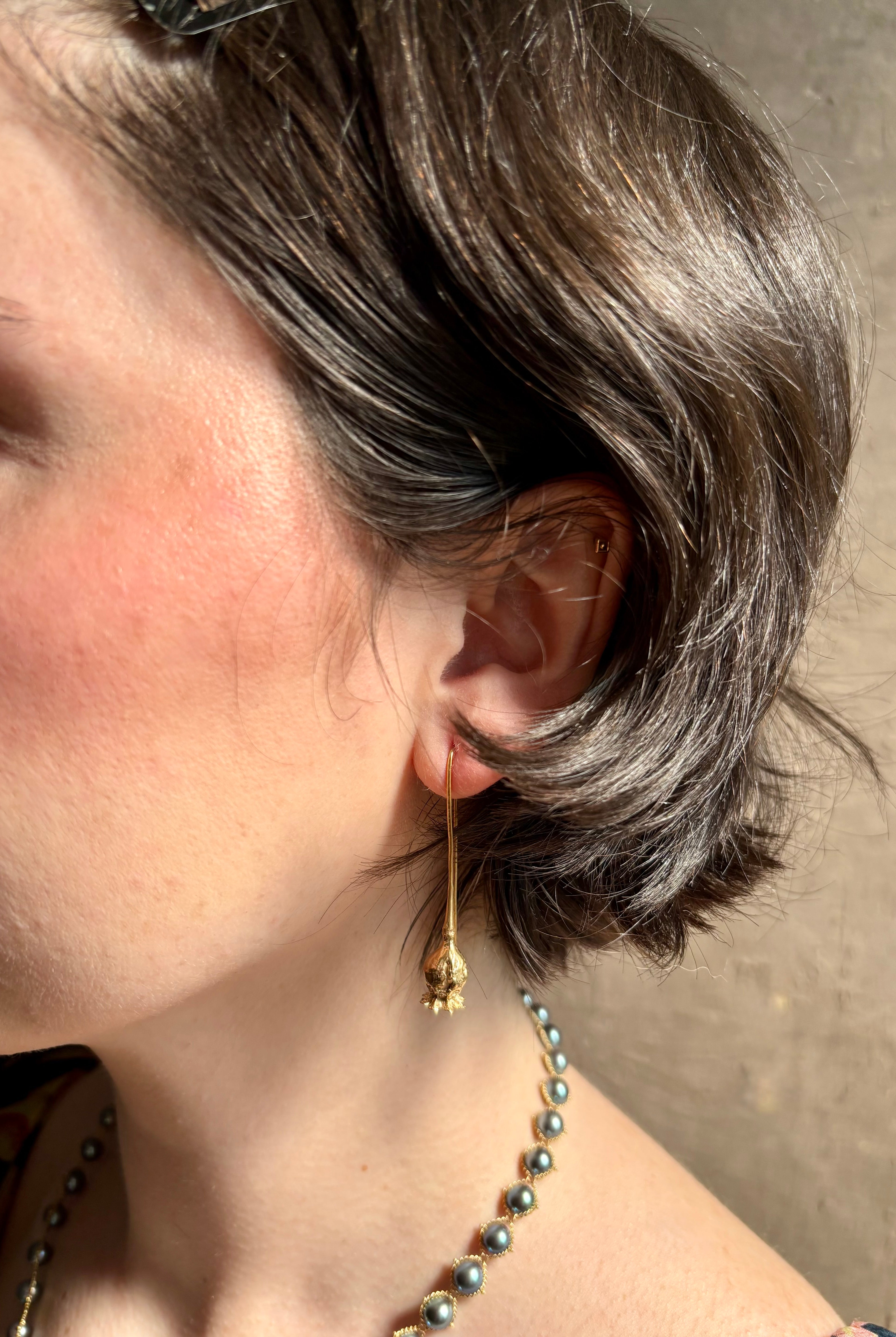 Woman wearing Poppy Pod Drop Earrings from North Carolina fine jewelry artist Amber Mahler handcrafted 18K yellow gold vermeil botanical casting