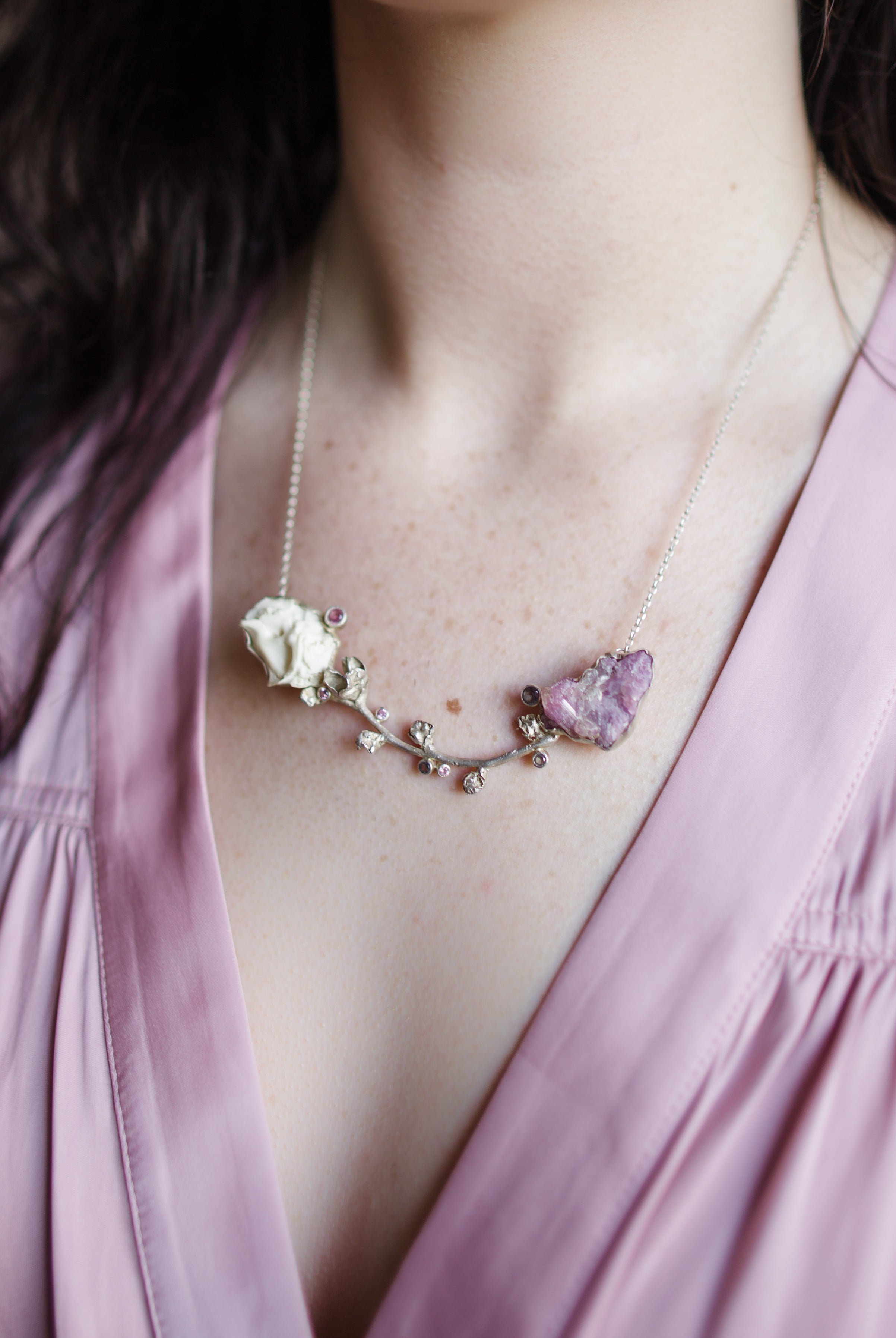 A woman wearing a silver cast brooch with a combination of Vesuvianite and tourmaline stones that can double as a necklace handmade in USA by North Carolina Jewelry artist Anna Johnson