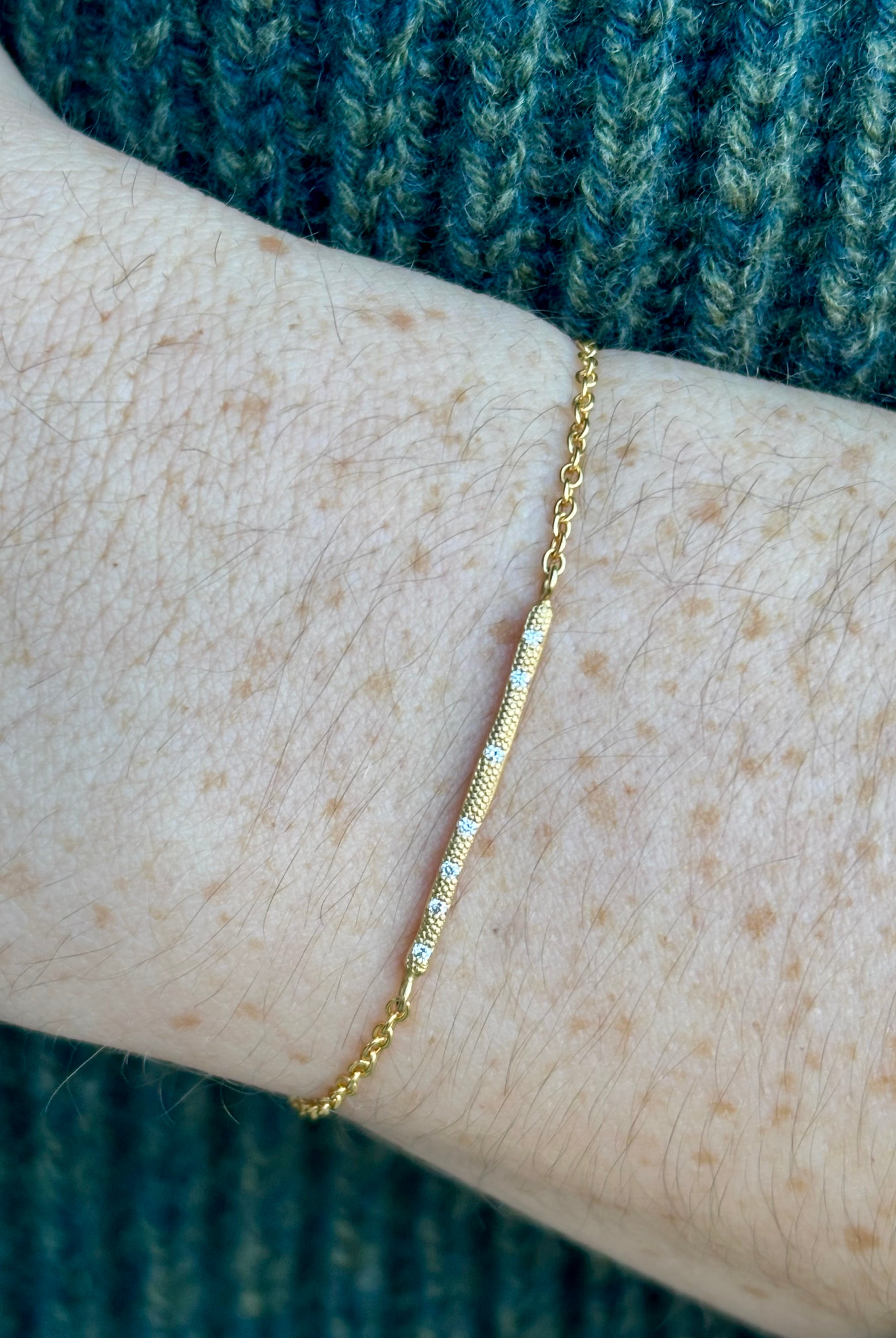 Image of a woman wearing designer Anne Sportun 18 carat gold diamond stardust bracelet single bar with hammered texture and adjustable clasp