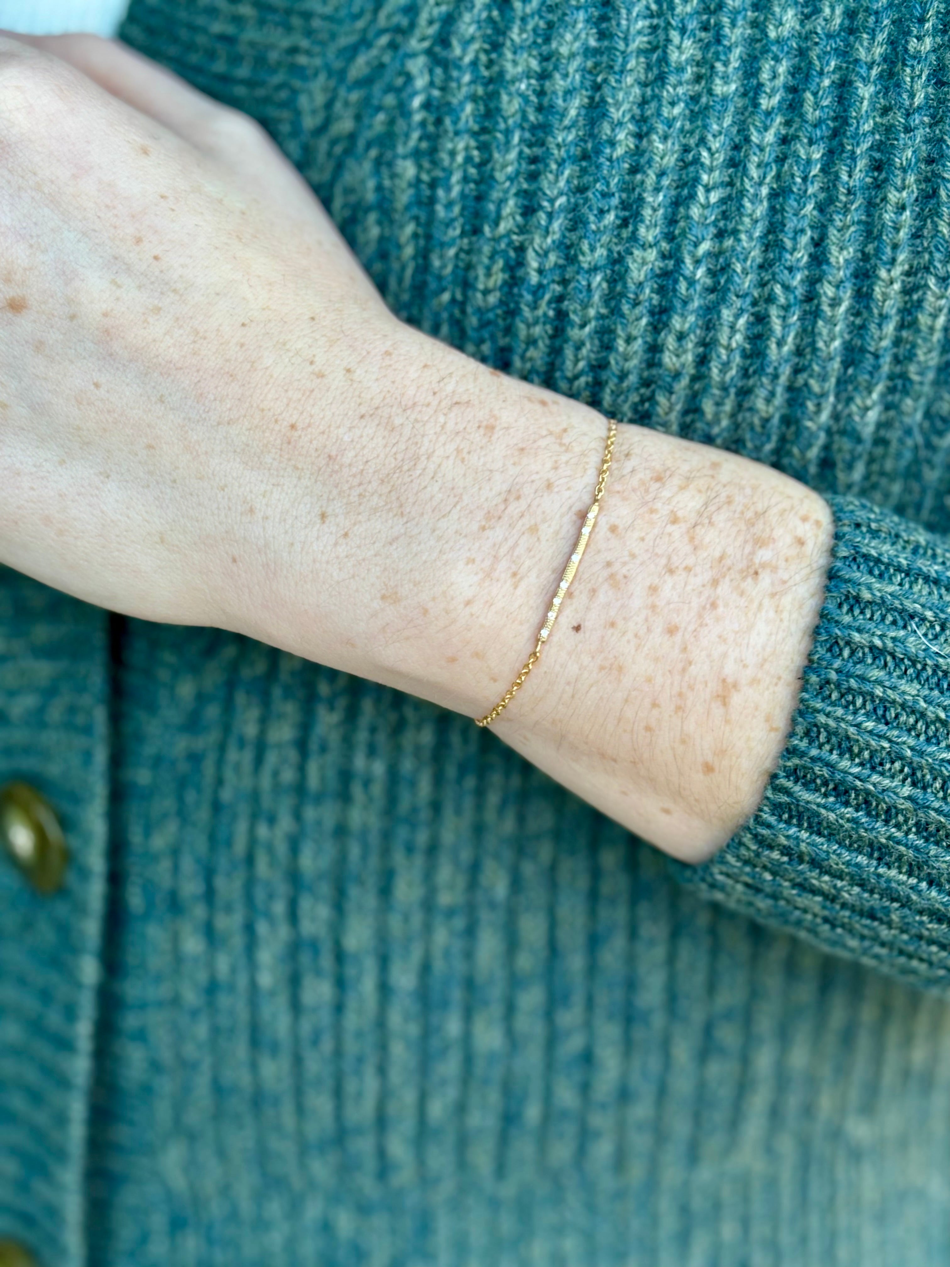 Image of a woman wearing designer Anne Sportun 18 carat gold diamond stardust bracelet single bar with hammered texture and adjustable clasp