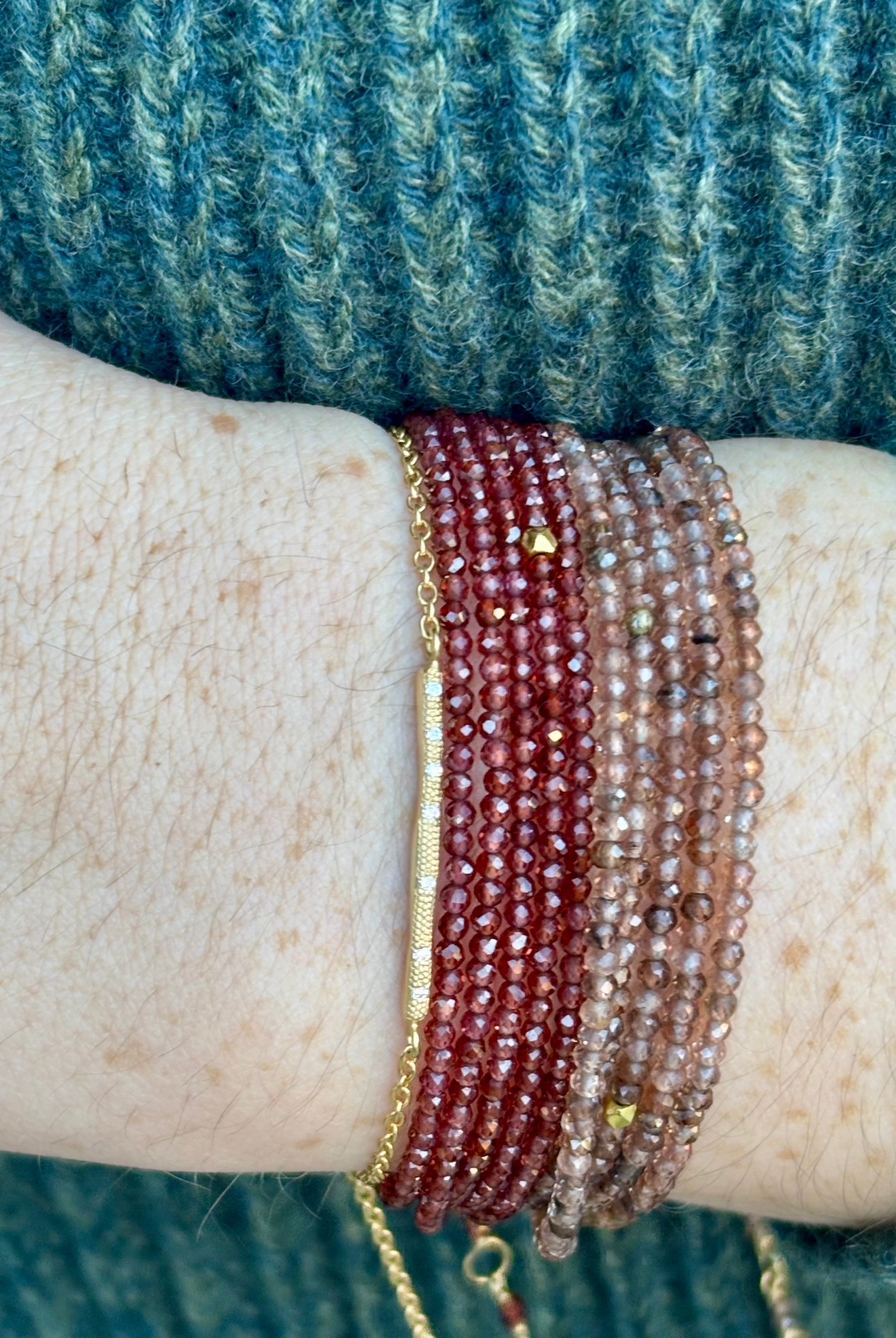 Image of woman wearing a stack of Canadian jewelry designer Anne Sportun bracelets with diamonds, 18k yellow gold and garnets