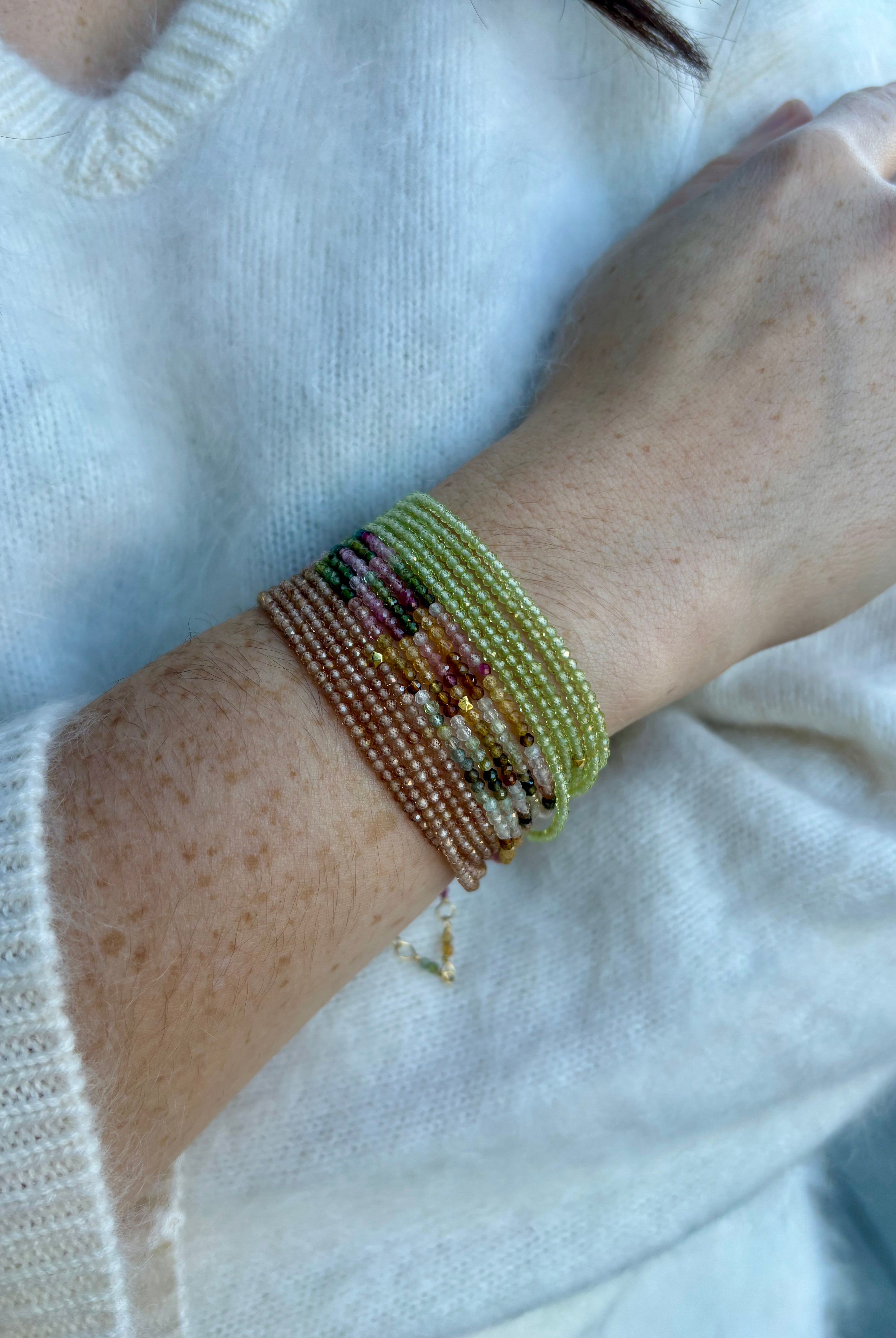 Image of a woman wearing premium jewelry stacked peridot, tourmaline, and garnet bracelets by Canadian designer Anne Sportun