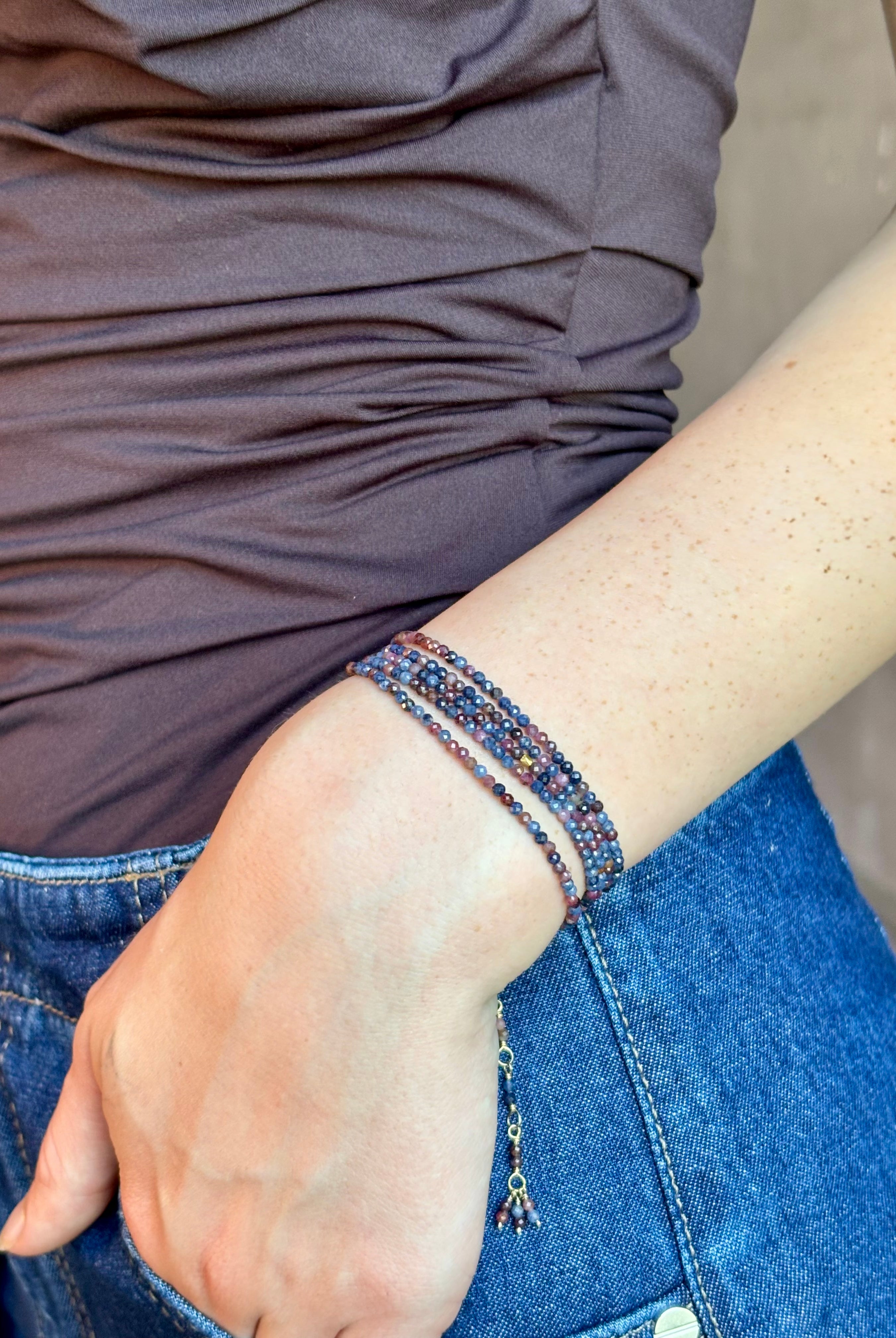 Woman wearing sapphire wrap Bracelet from Canadian fine jewelry artist Anne Sportun with natural multi-colored sapphires and 18k yellow gold that can double as a necklace perfect for travel
