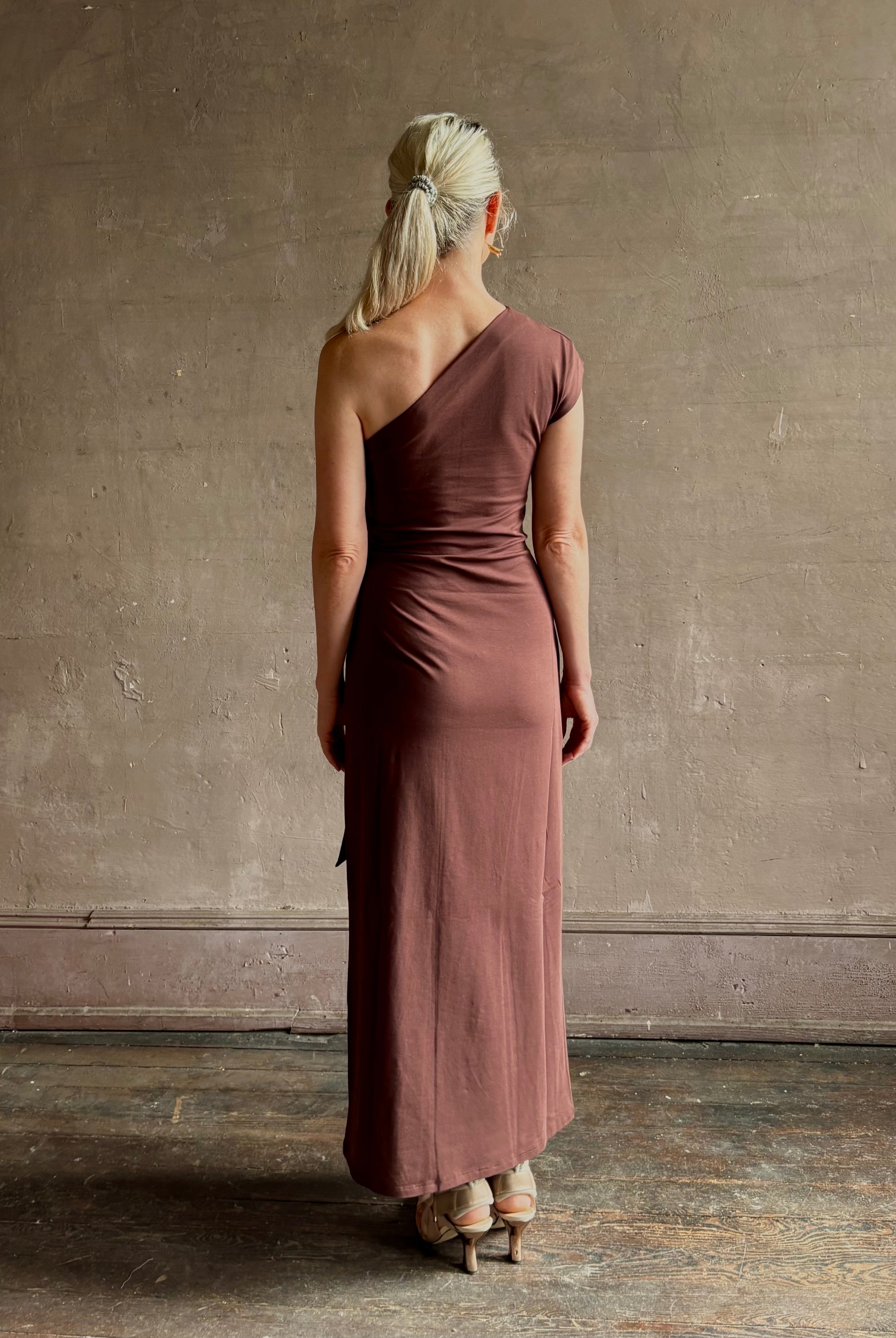 Mature woman wearing Apiece Apart brown comfy jersey cotton maxi dress one shoulder twist tie waist stretch