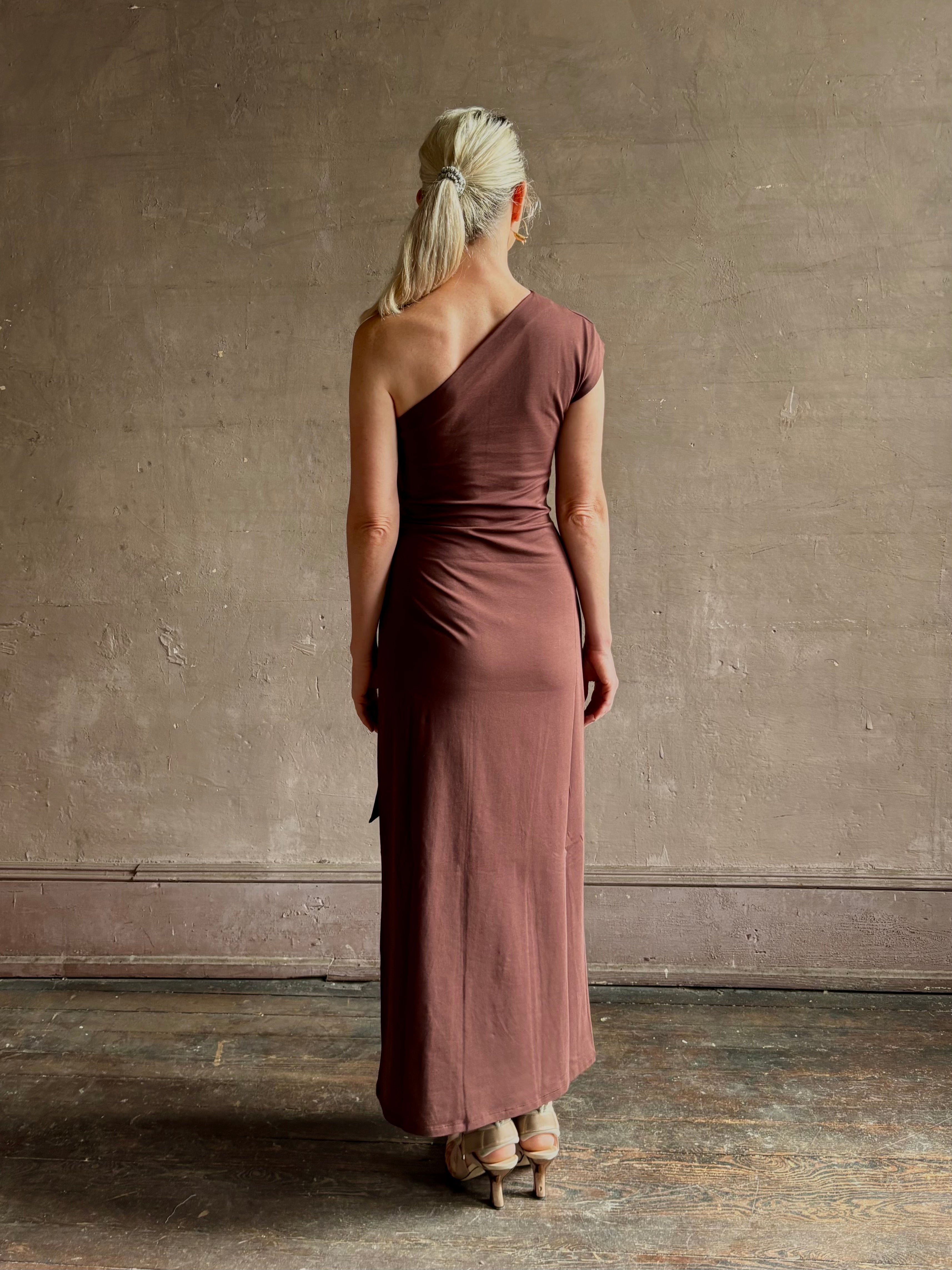 Mature woman wearing Apiece Apart brown comfy jersey cotton maxi dress one shoulder twist tie waist stretch