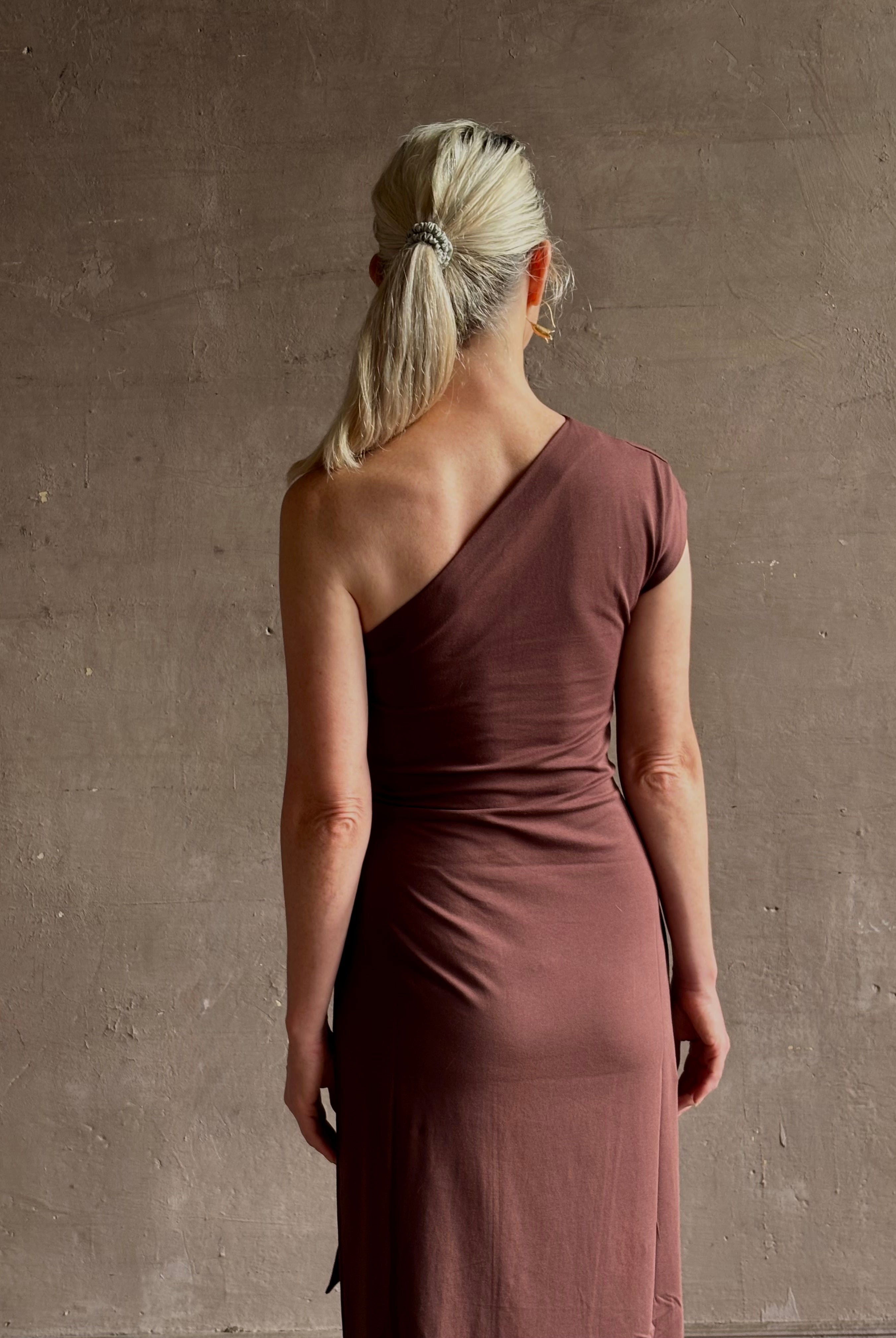 Mature woman wearing Apiece Apart brown comfy jersey cotton maxi dress one shoulder twist tie waist stretch