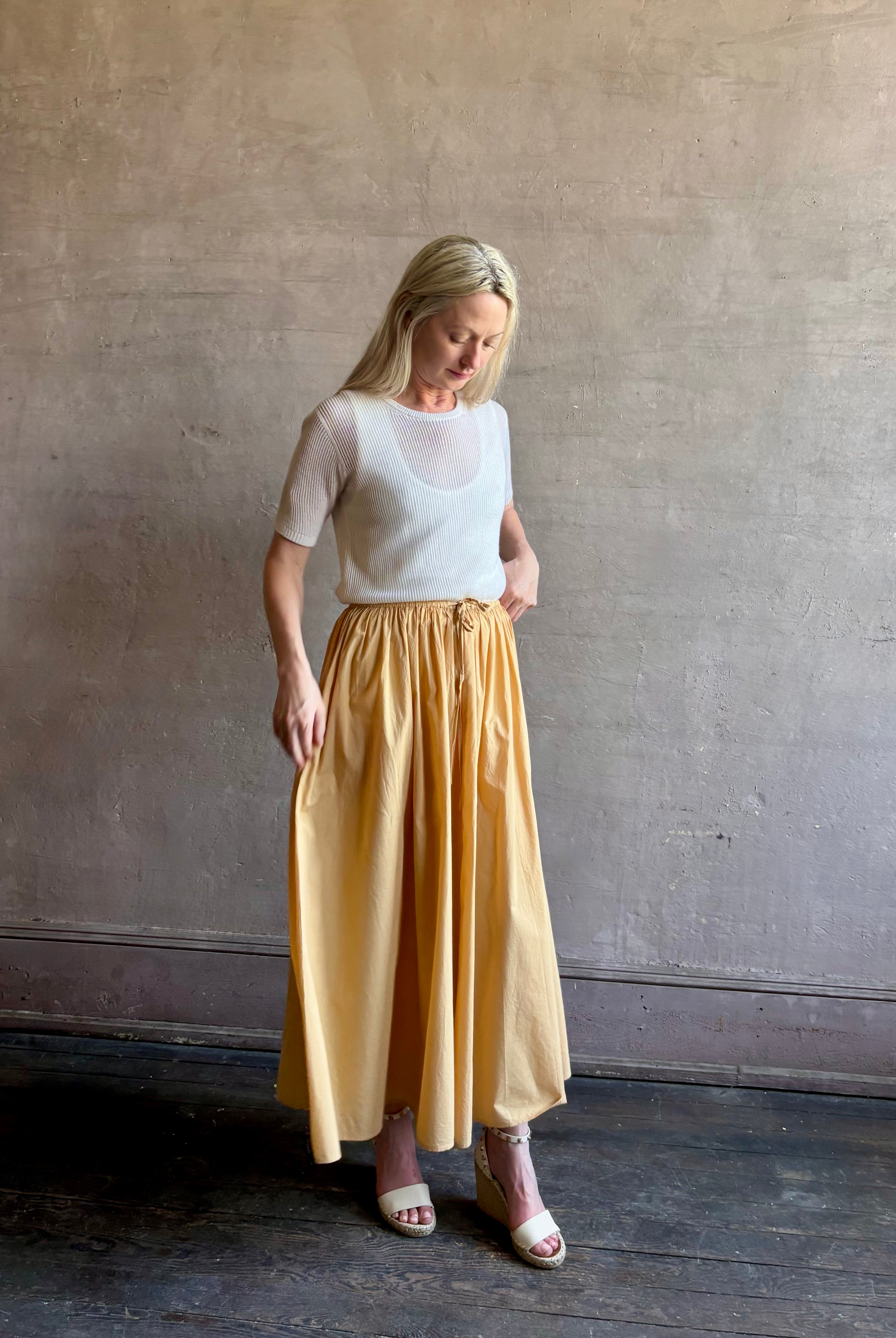 Mature woman wearing the Hanne Tie Maxi Skirt from Apiece Apart rendered in a butter yellow hue and crafted from 100% organic cotton with adjustable drawstring and elastic waistband