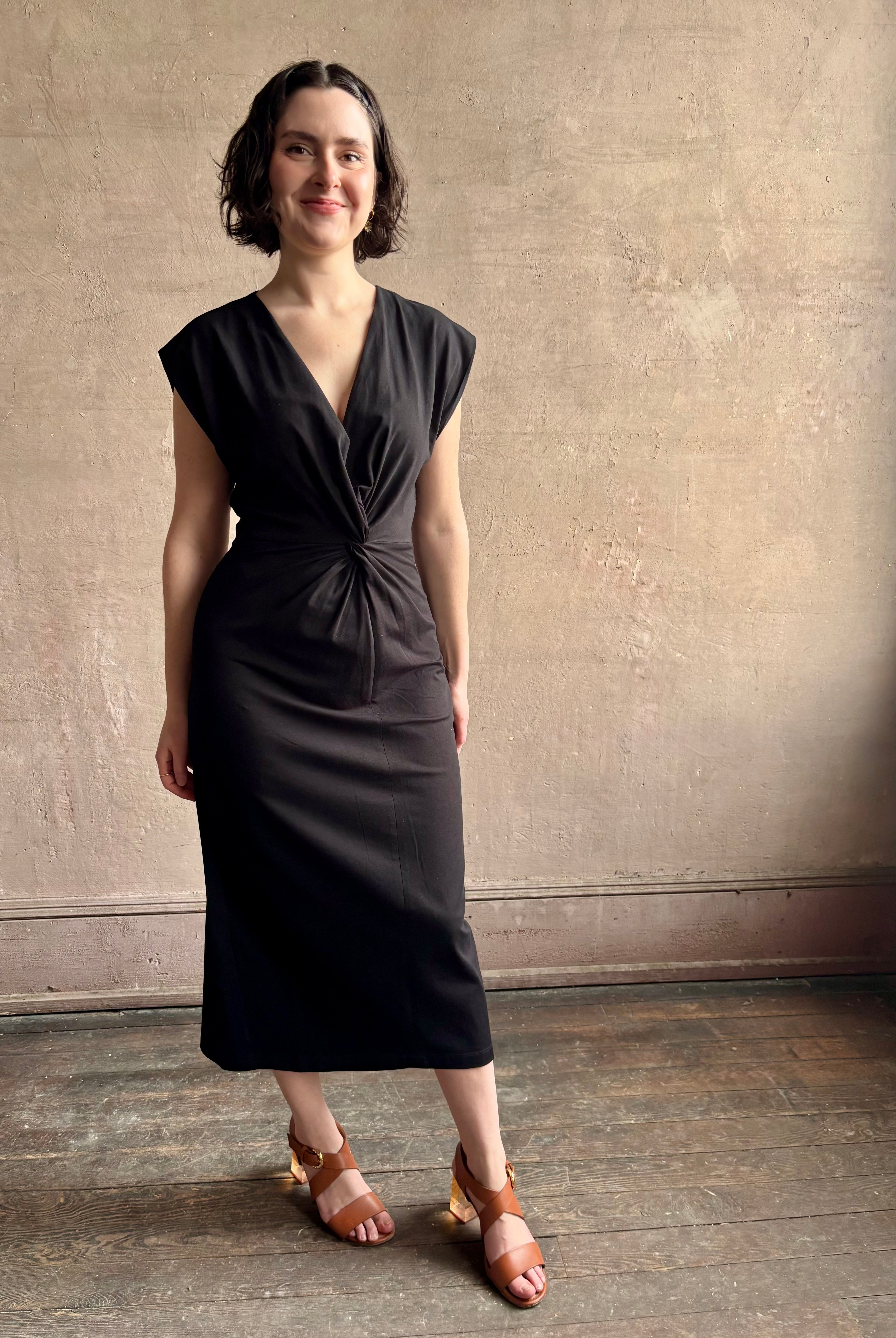 Woman wearing a timeless Twist Front Column Dress from Apiece Apart in a comfortable black cotton jersey midi that can transition day to night