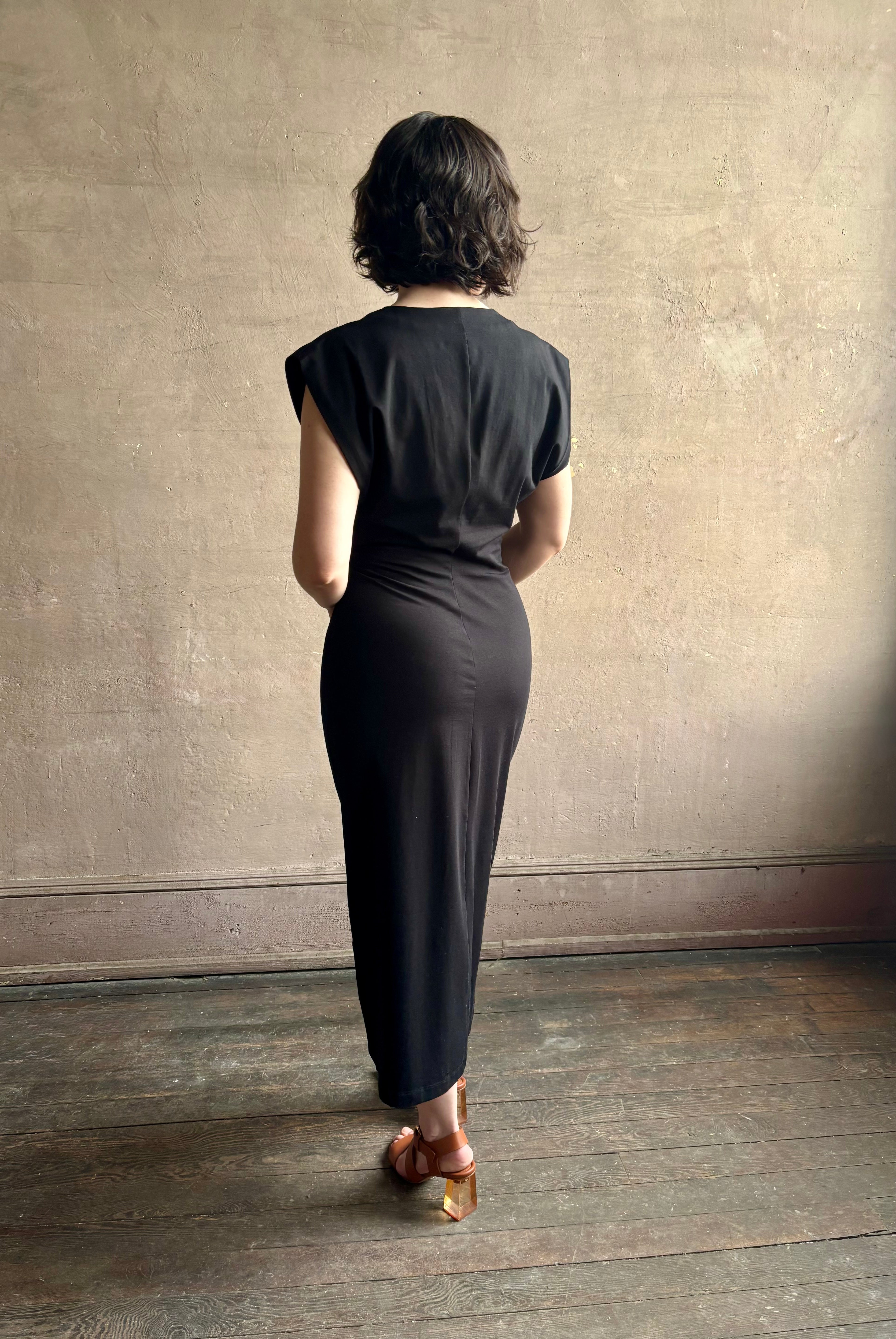 Woman wearing a timeless Twist Front Column Dress from Apiece Apart in a comfortable black cotton jersey midi that can transition day to night