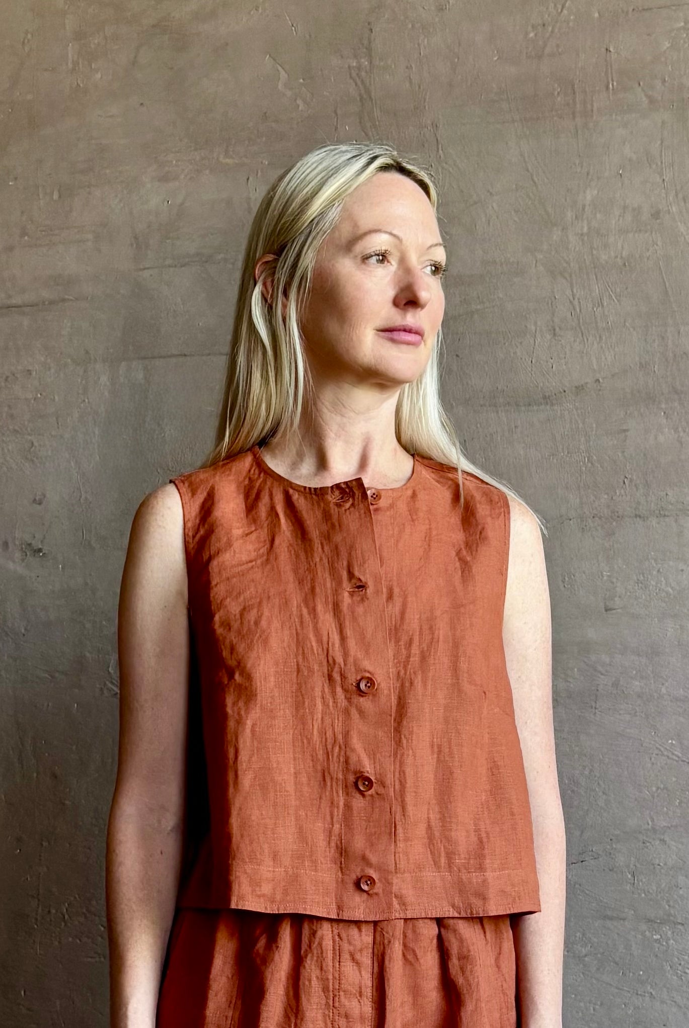 Mature woman wearing the Mar Short from Apiece Apart rendered in a rust hue and crafted from 100% linen with an adjustable elastic waistband and pockets and matching top set