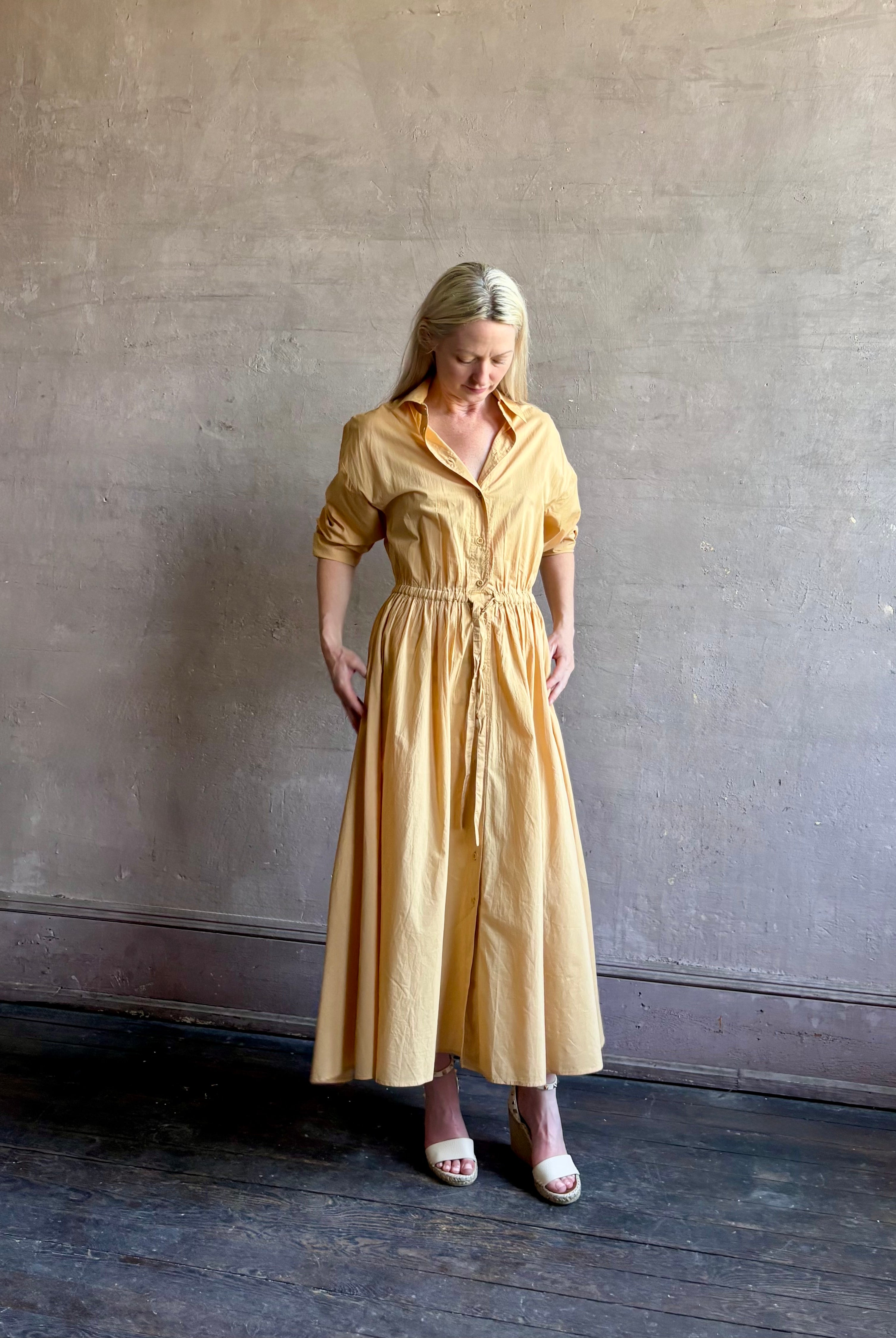 Image of mature woman wearing the Priska Shirt Dress from Apiece Apart rendered in a butter yellow and crafted from 100% organic cotton featuring long sleeves, collared button front and adjustable drawstring waistband