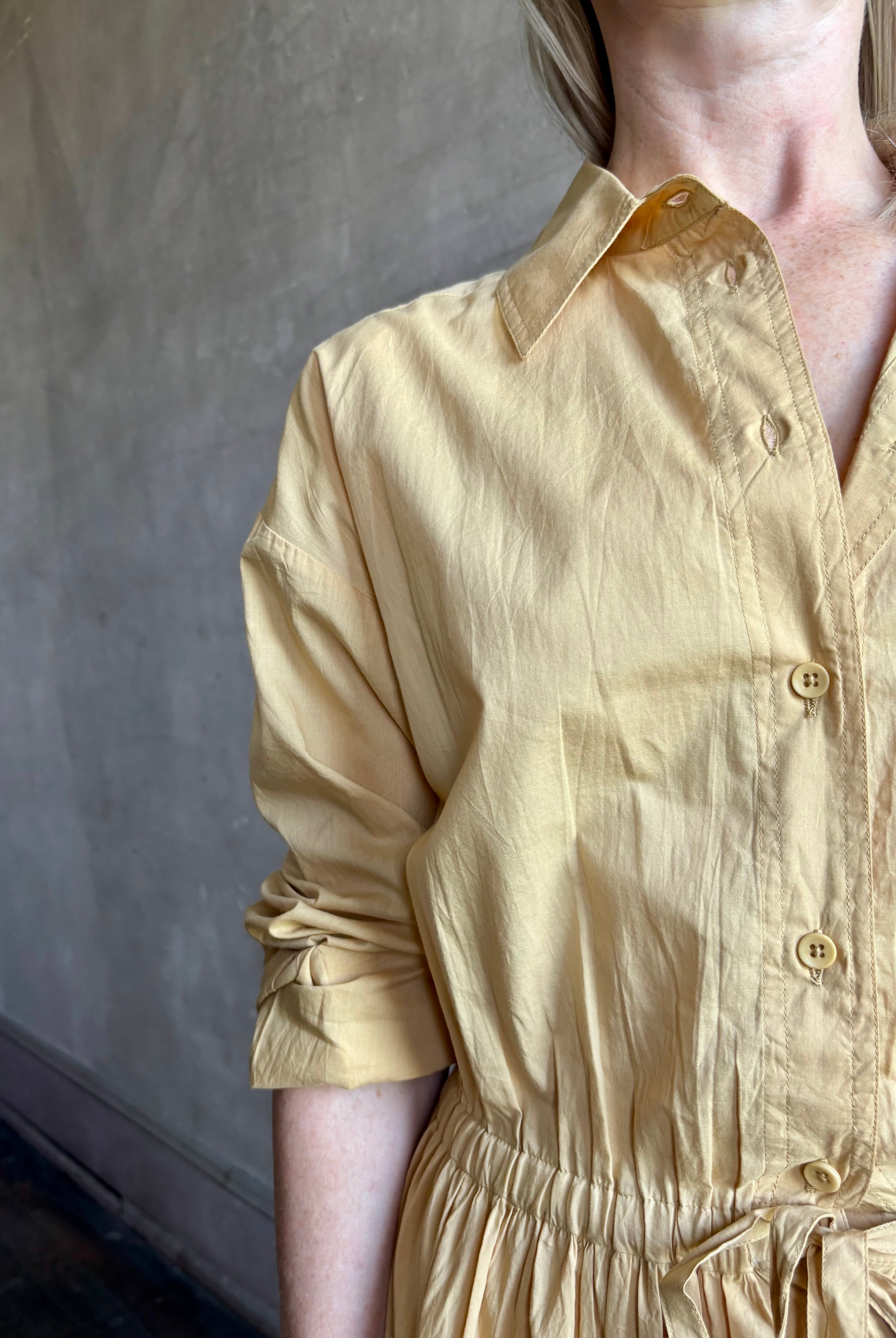 Image of mature woman wearing the Priska Shirt Dress from Apiece Apart rendered in a butter yellow and crafted from 100% organic cotton featuring long sleeves, collared button front and adjustable drawstring waistband