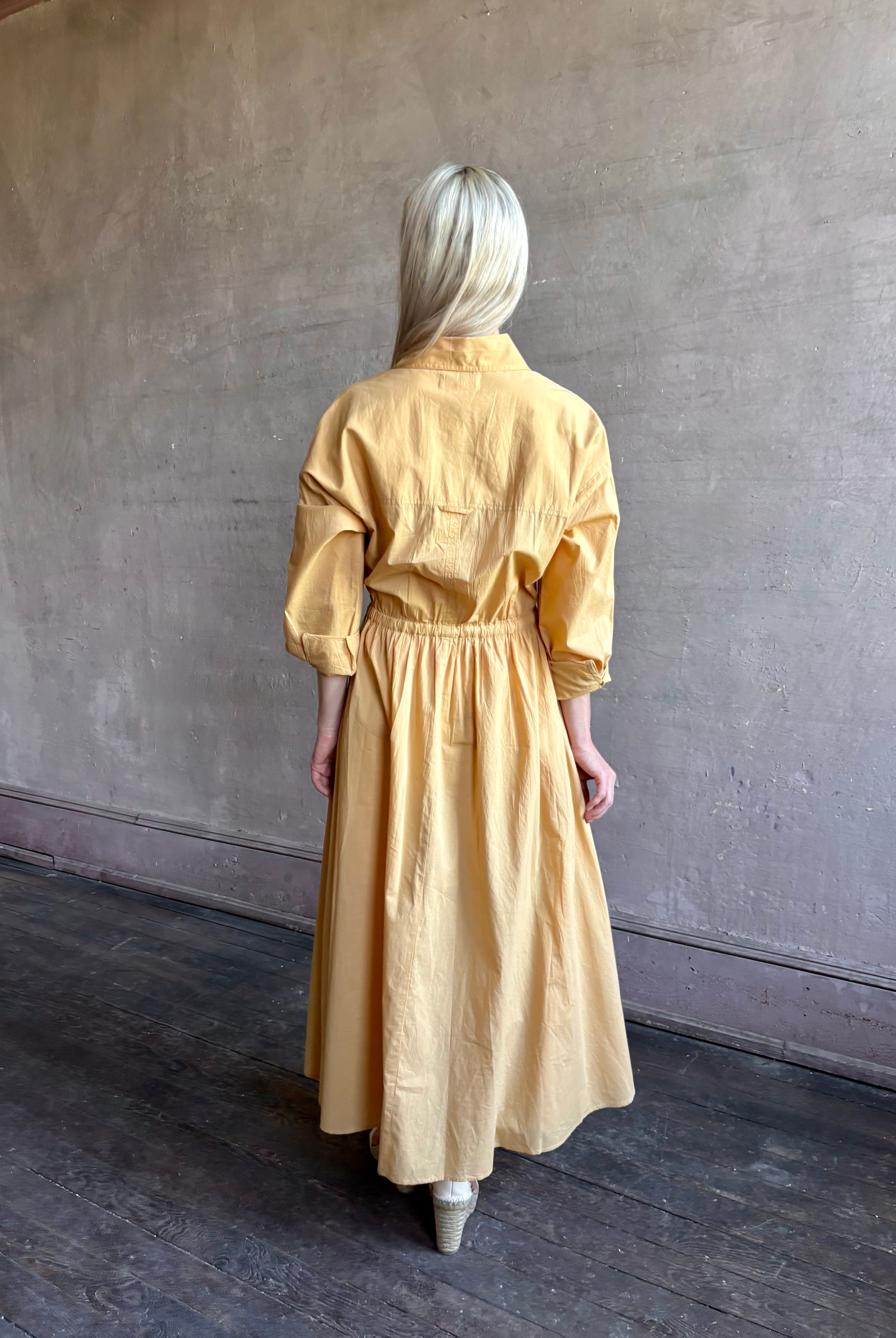 Image of mature woman wearing the Priska Shirt Dress from Apiece Apart rendered in a butter yellow and crafted from 100% organic cotton featuring long sleeves, collared button front and adjustable drawstring waistband