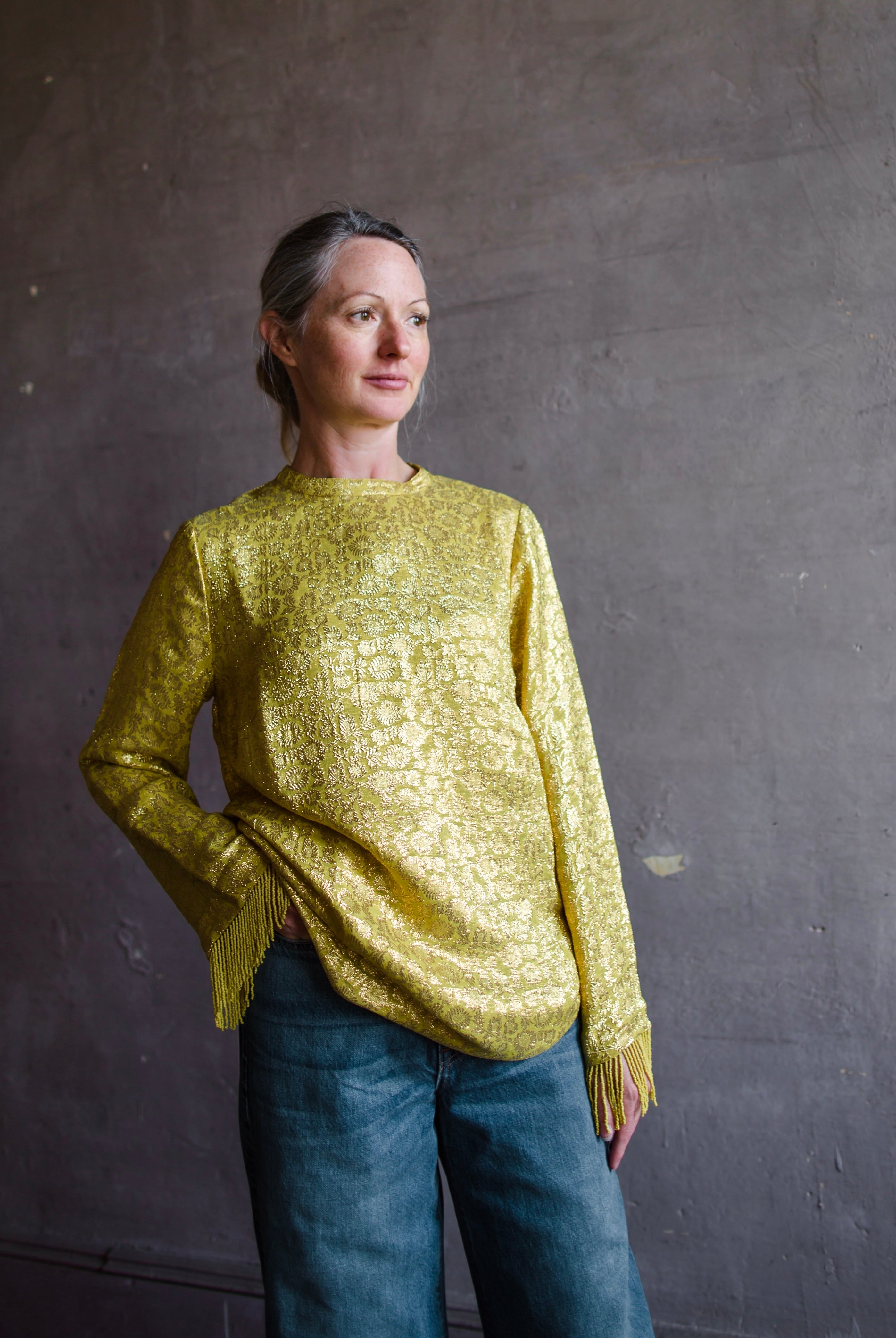 Image featuring a woman wearing the yellow Astra top by Alemais features a crew neckline with brocade texture and beaded fringe trim.
