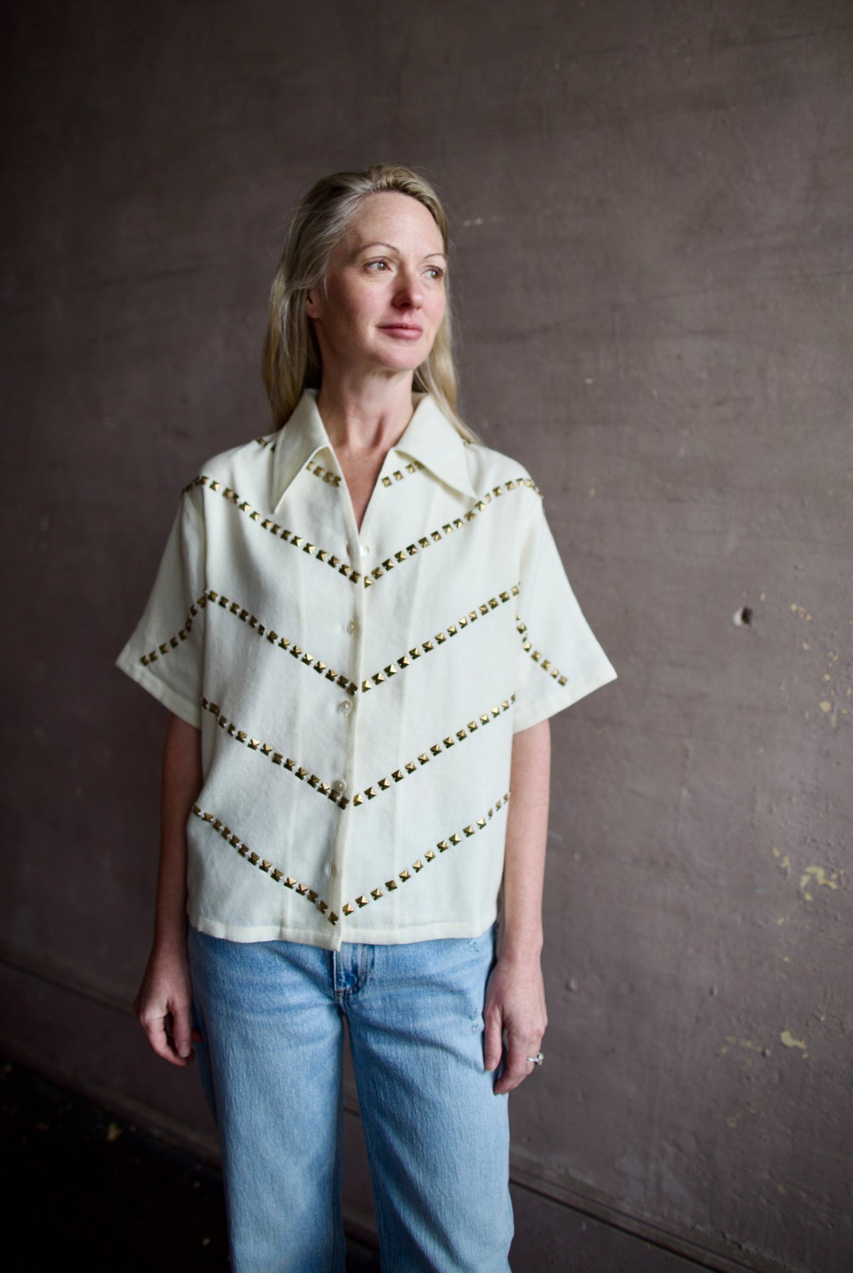 Mature woman wearing Alix of Bohemia Stevie Studded top with button front short sleeves and a collar metal embellishments in V design across entire front