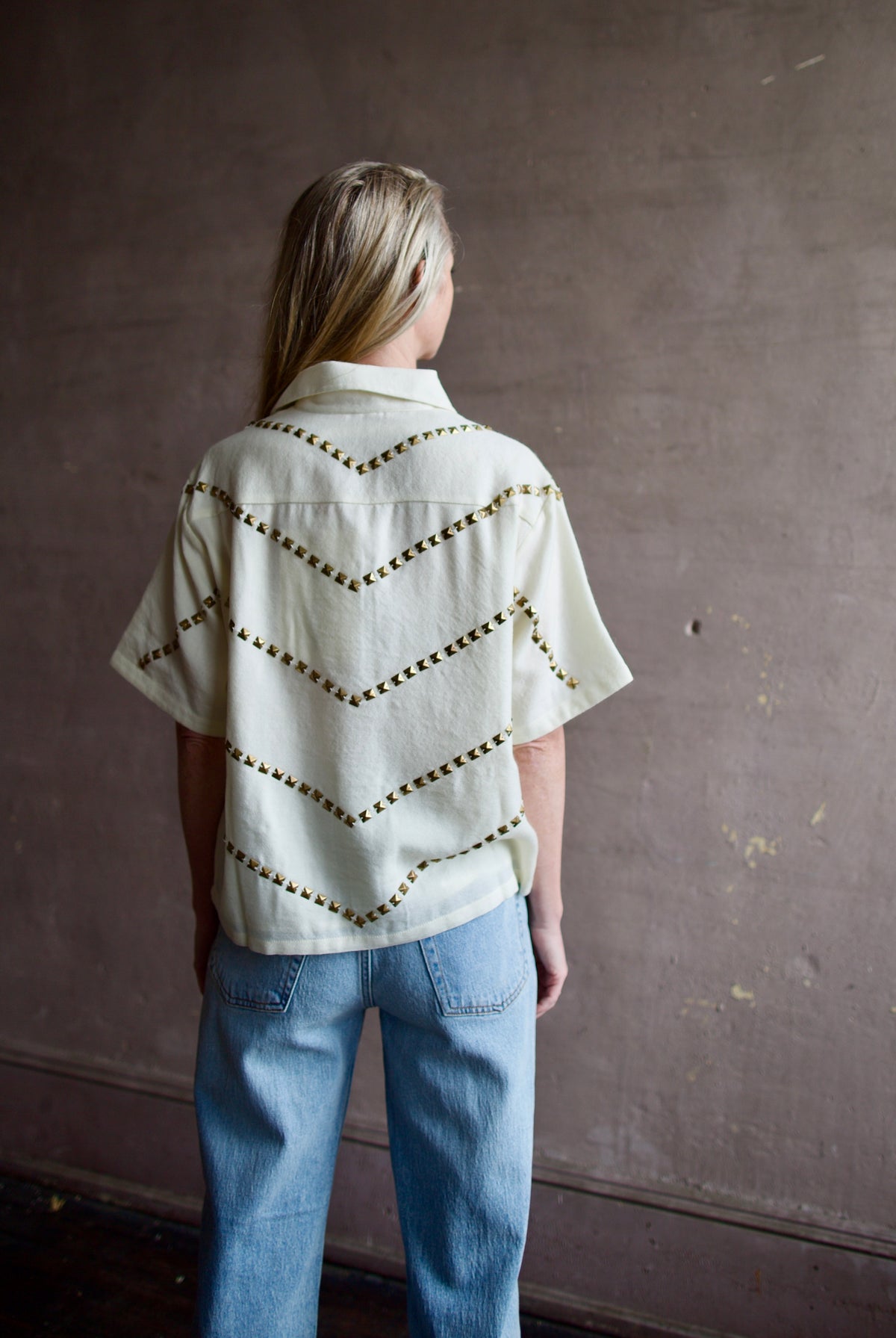 Mature woman wearing Alix of Bohemia Stevie Studded top with button front short sleeves and a collar metal embellishments in V design across entire back