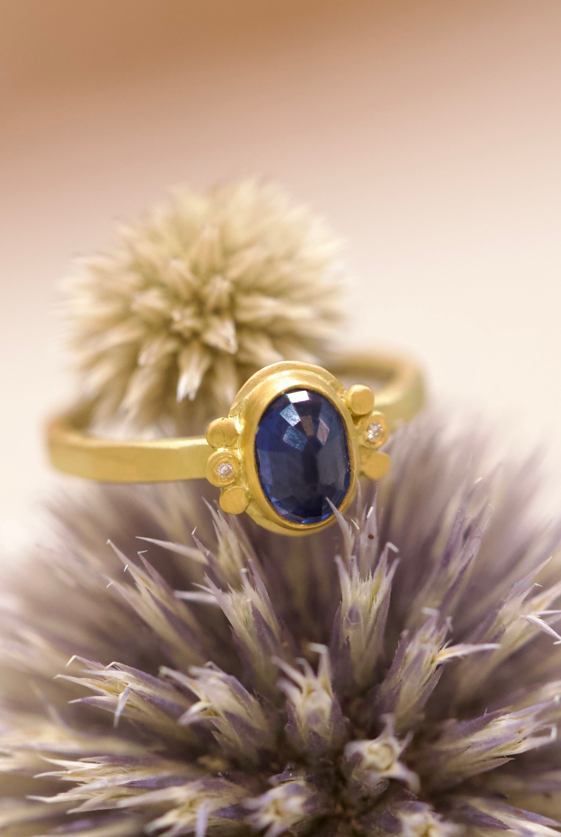 Image of handmade rosecut oval blue sapphire ring by Ananda Khalsa designed with a 22kt gold bezel, 18kt gold band, and 22kt gold diamond trios.