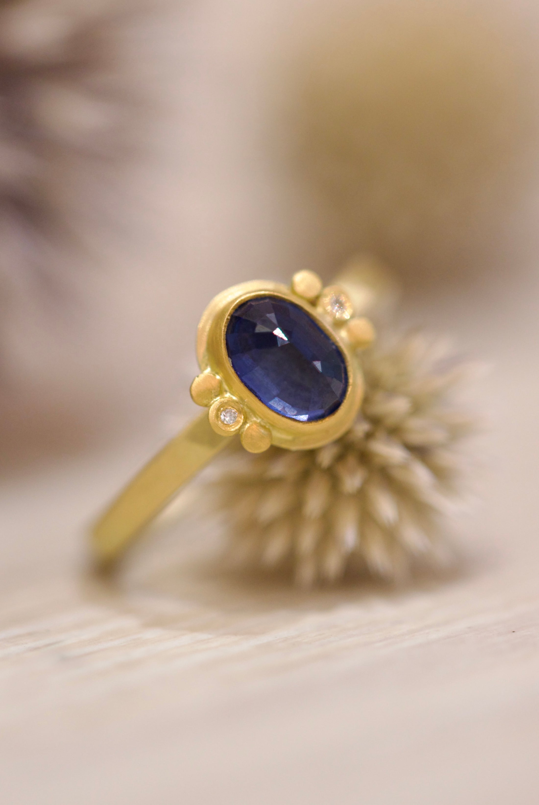 Image of handmade rosecut oval blue sapphire ring by Ananda Khalsa designed with a 22kt gold bezel, 18kt gold band, and 22kt gold diamond trios.