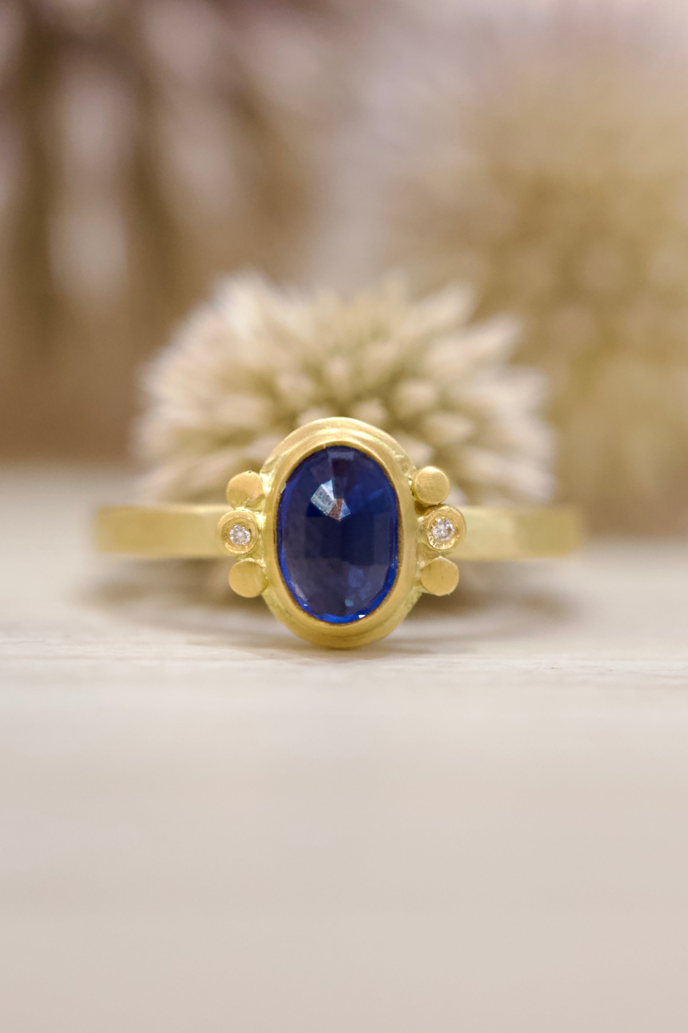 Image of handmade rosecut oval blue sapphire ring by Ananda Khalsa designed with a 22kt gold bezel, 18kt gold band, and 22kt gold diamond trios.
