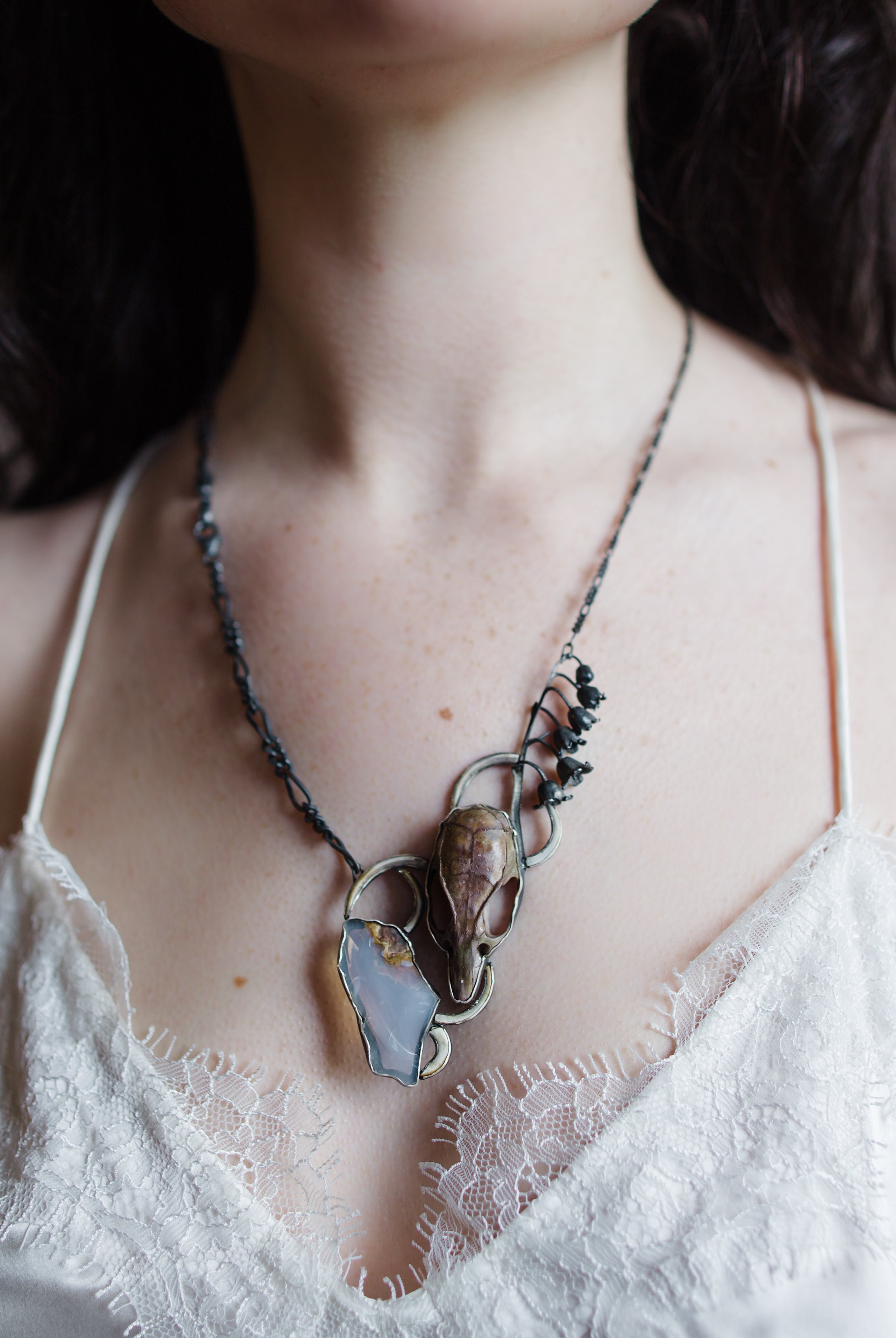Image featuring a woman wearing North Carolina artist Anna Johnson Inciroda Necklace with Rat skull, rodent incisors, Oregon opal, silver and lily of the valley casting