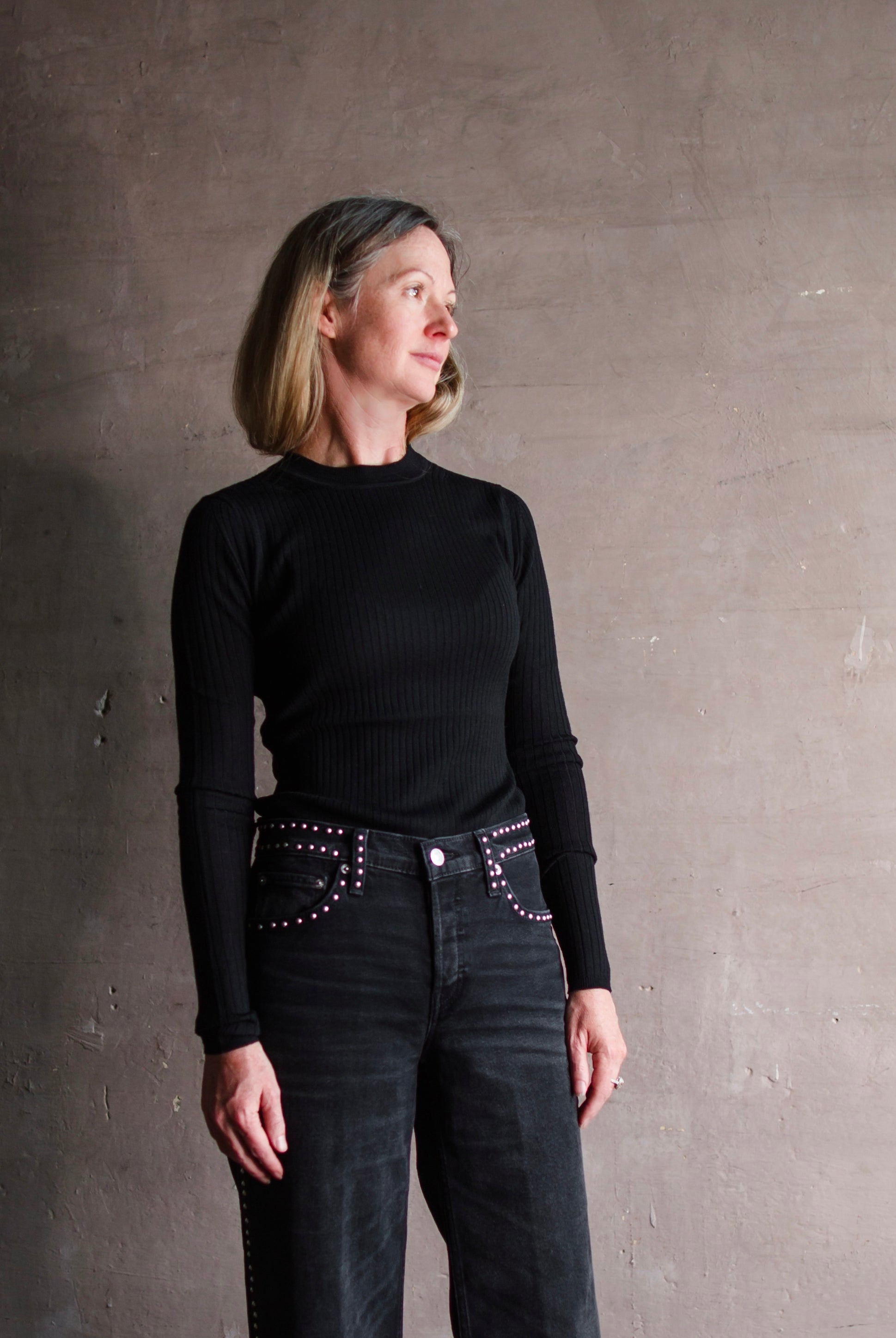 Image featuring a woman wearing the sweater top by Apiece Apart merino wool with a crew neckline, ribbed texture and a tailored fit in black