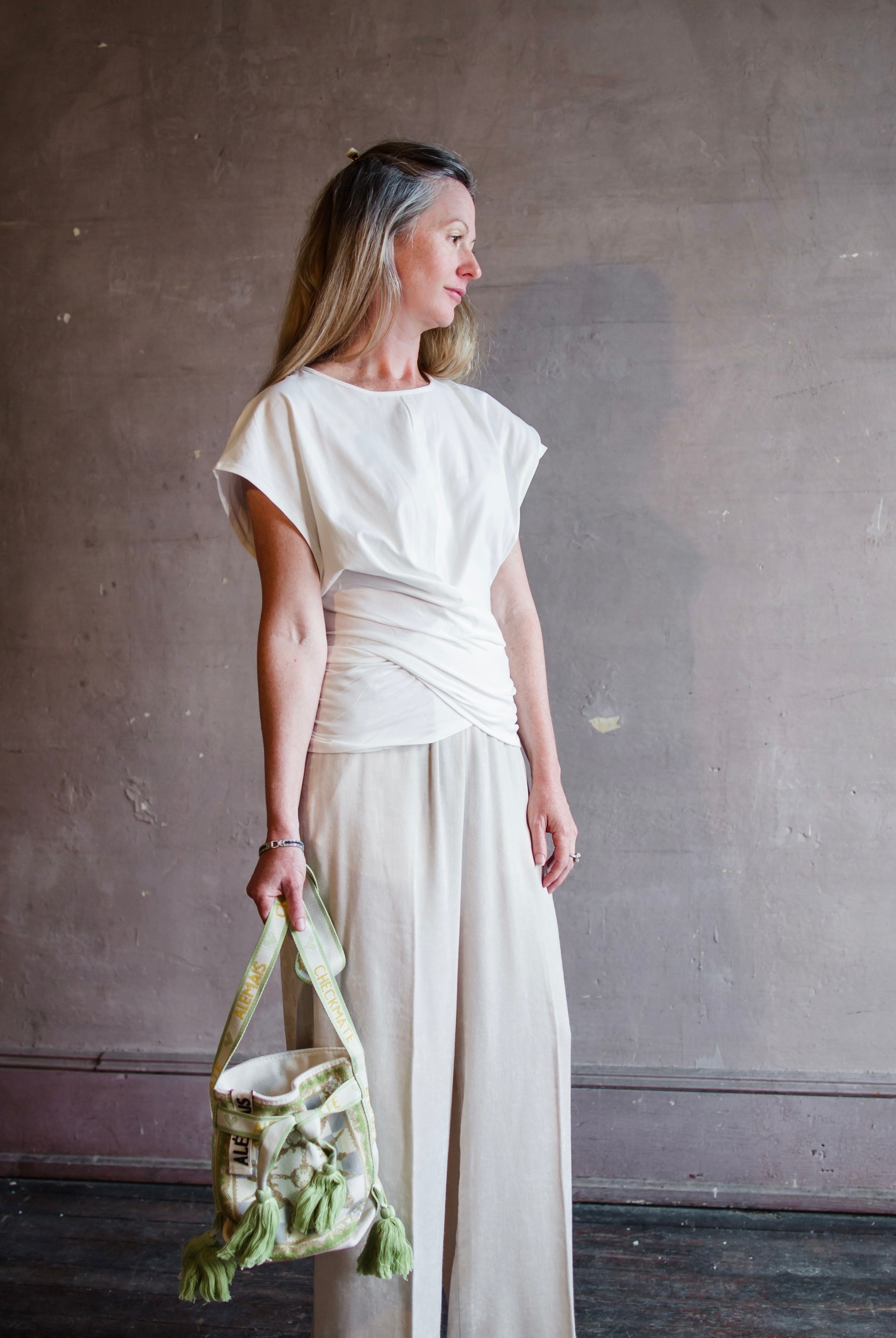 Image featuring a woman wearing the twist top by Apiece Apart with a crew neckline, cap sleeve and a flattering twist at the waist in white