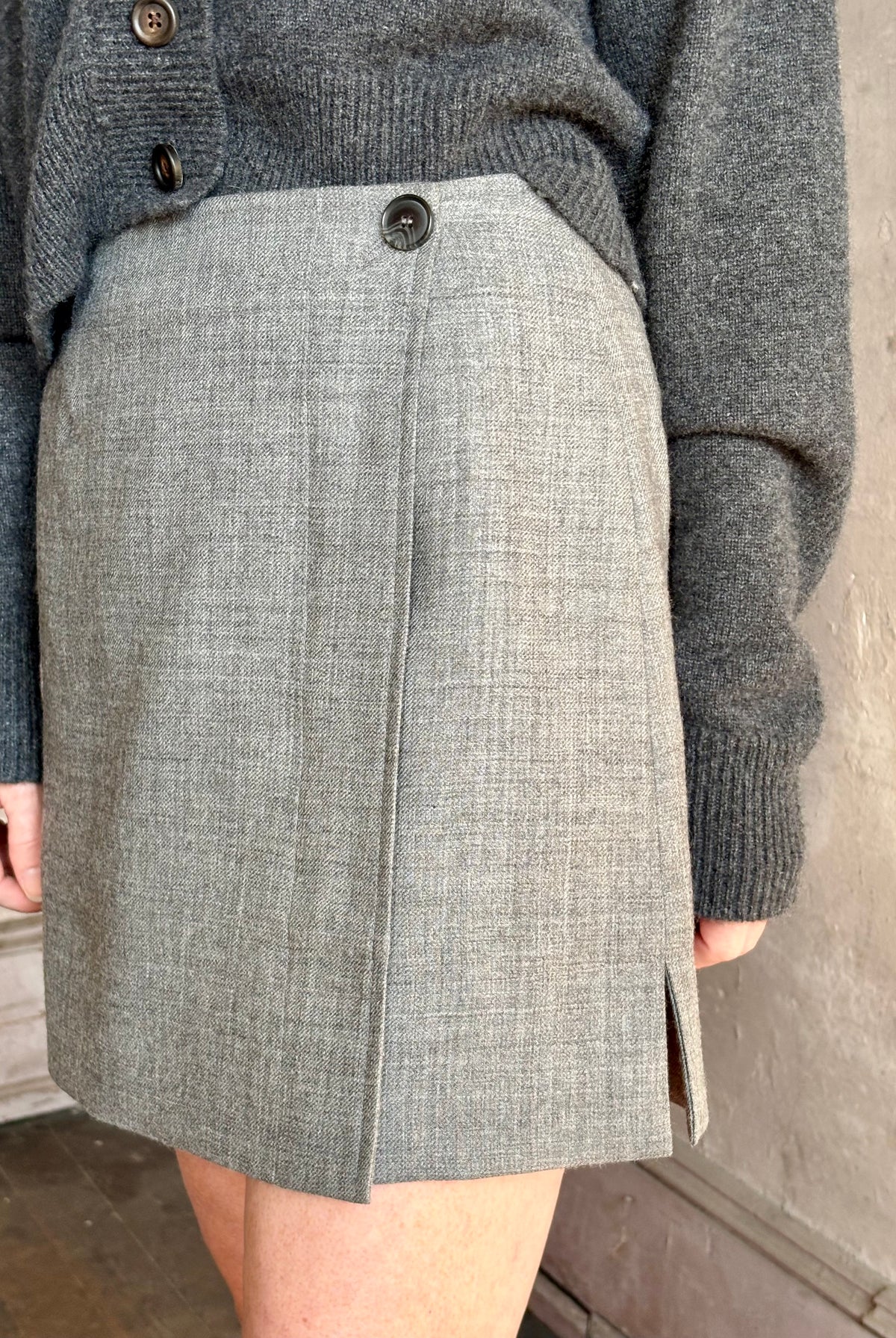 Close up image of mature woman wearing Apiece Apart gray textured Marta mini skirt with a front button closure and side vent tailoring