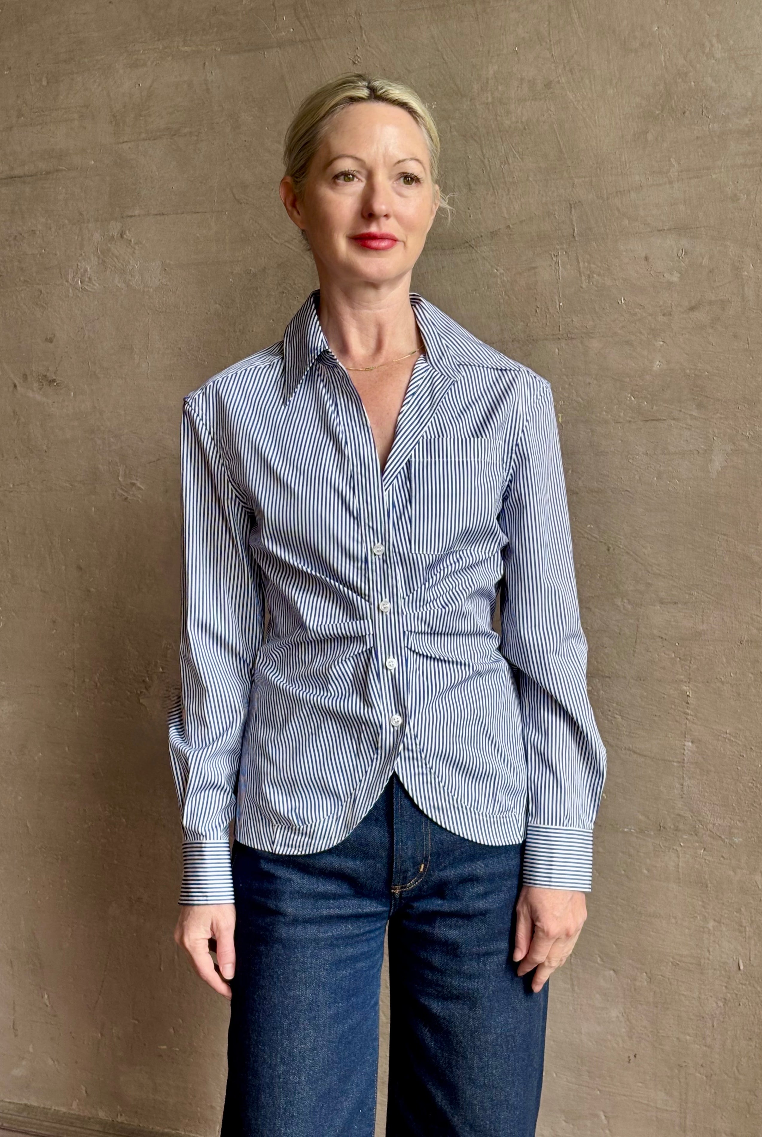 Mature woman wearing the European tailored Sierra Shirt from Callas rendered in a crisp navy and white stripe and crafted from cotton poplin featuring a flattering ruched front , long sleeves, v-neck and rounded bottom detail